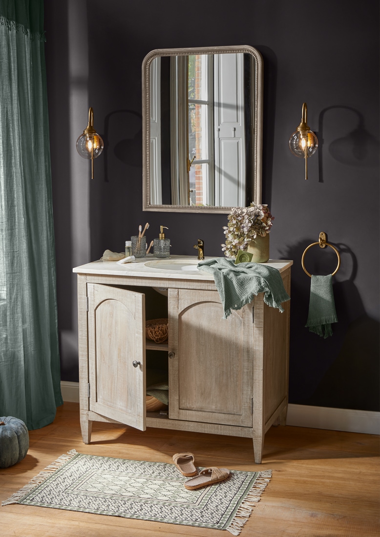 Meuble de salle de bain en bois clair avec miroir, accessoires dorés et serviette verte, style vintage