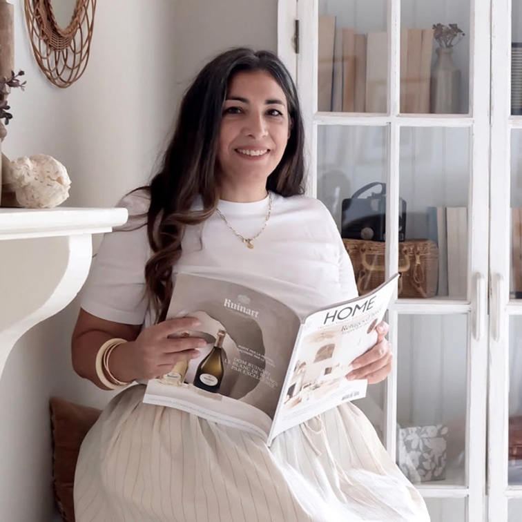 Femme en haut blanc et jupe claire lisant un magazine de décoration dans une pièce lumineuse avec une armoire en bois