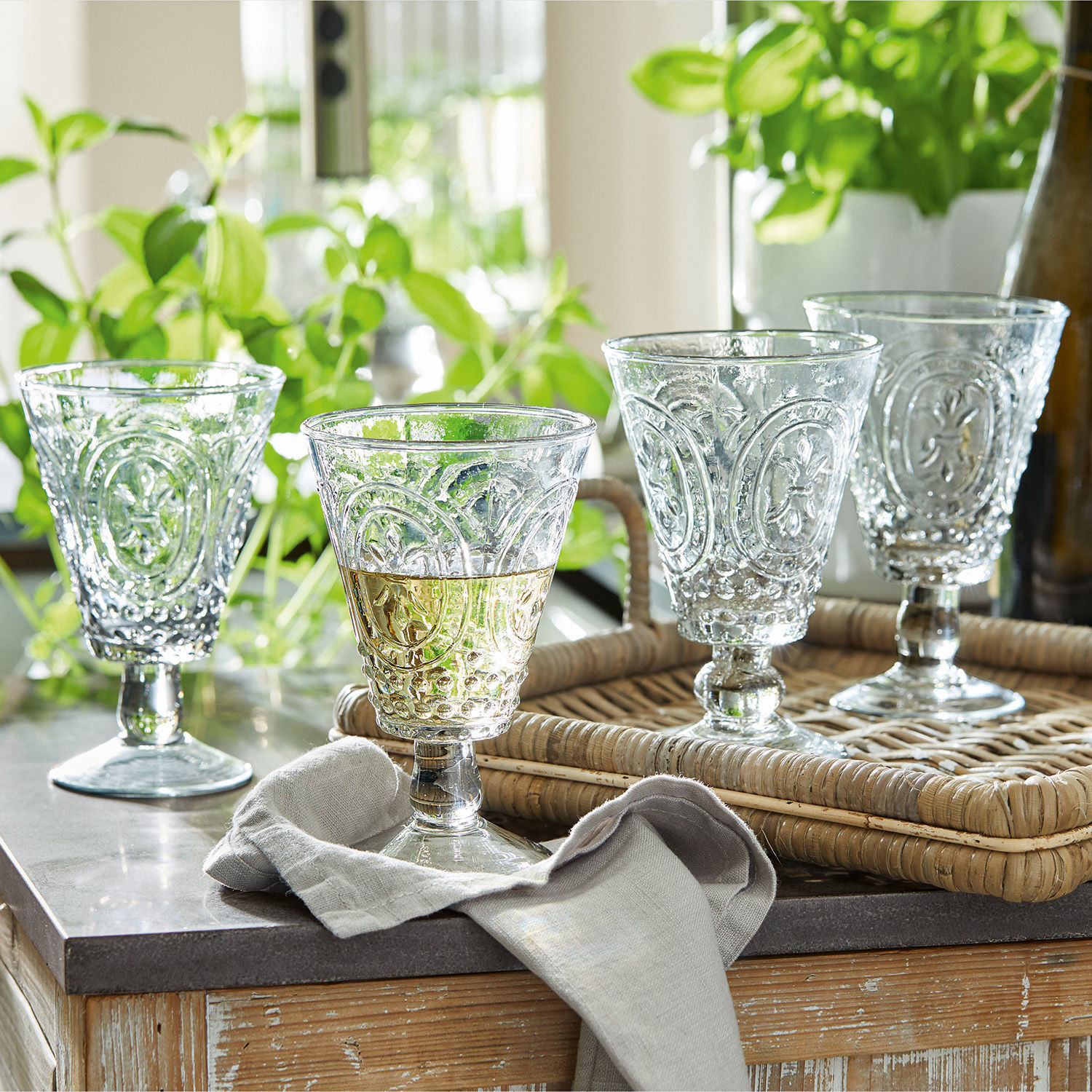 Lot de 4 verres à vin Sarton Ensemble de quatre verres transparents avec motif décoratif sur un plateau en rotin sur une table