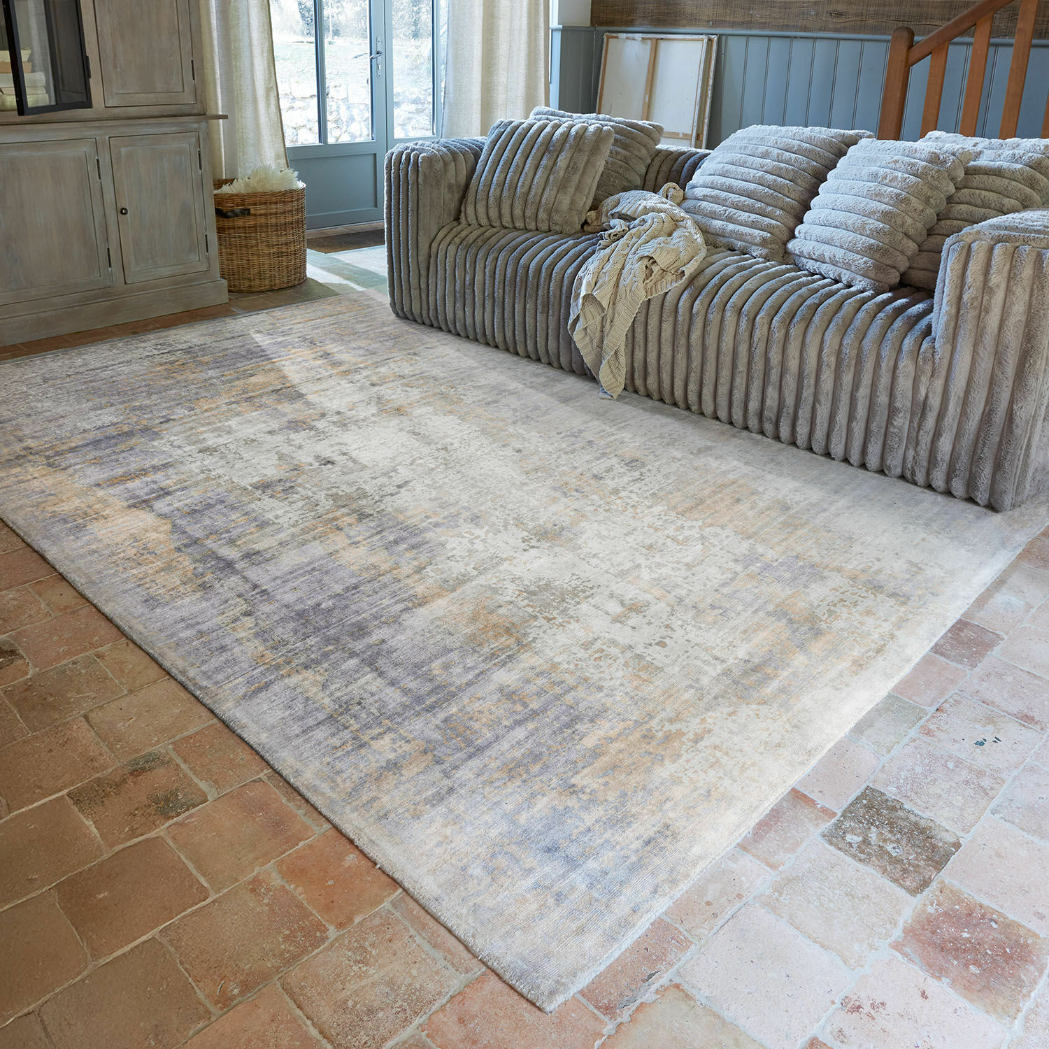 Grand tapis beige et gris sur sol en briques dans un salon chaleureux avec canapé gris côtelé