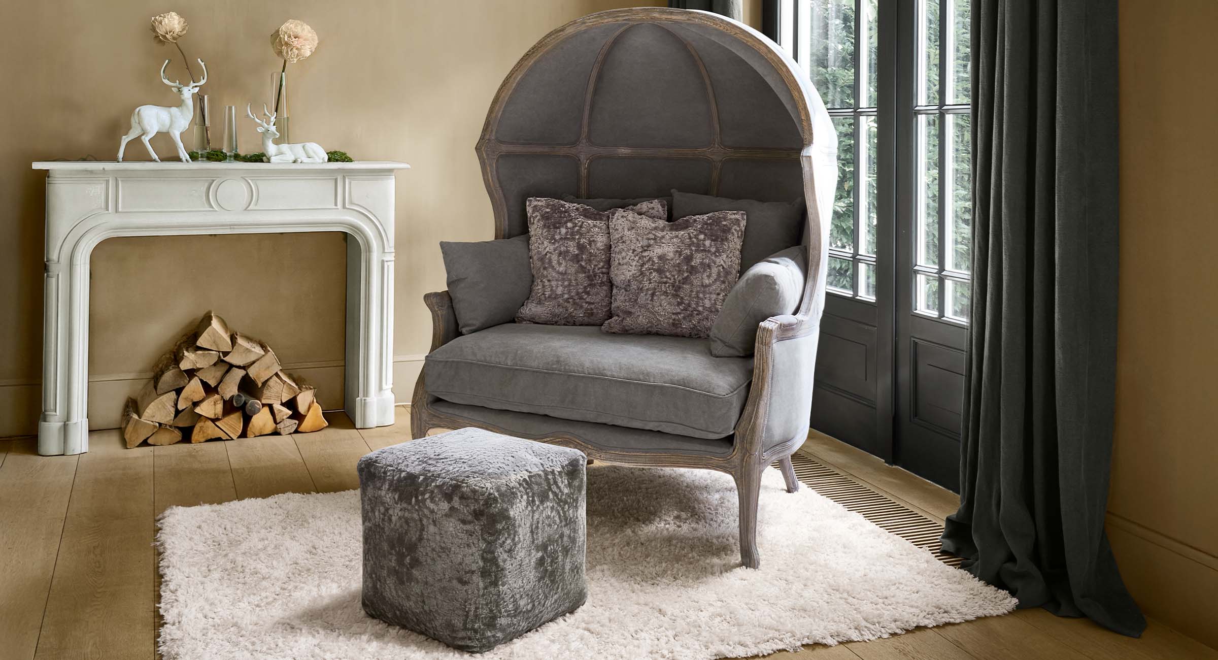 Fauteuil boule gris en velours avec cadre en bois et pouf assorti sur tapis blanc dans un salon cosy