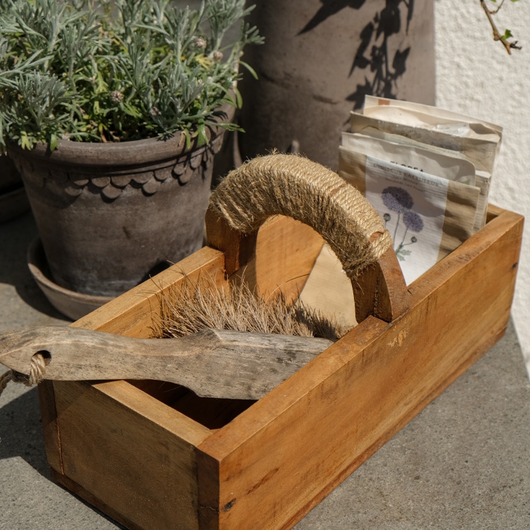 Boîte en bois avec poignée en corde, contenant une brosse et des sachets de graines, matériaux naturels
