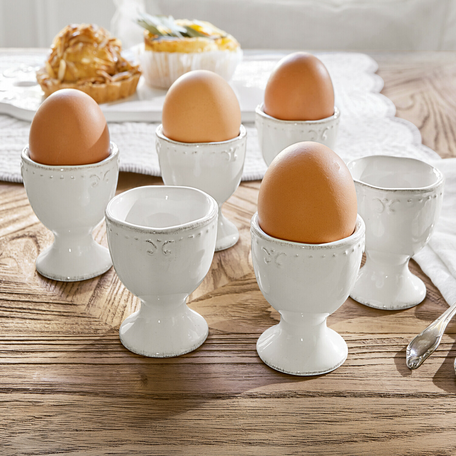 Lot de 6 coquetiers Fontienne Ensemble de coquetiers en céramique blanche avec œufs bruns sur table en bois clair