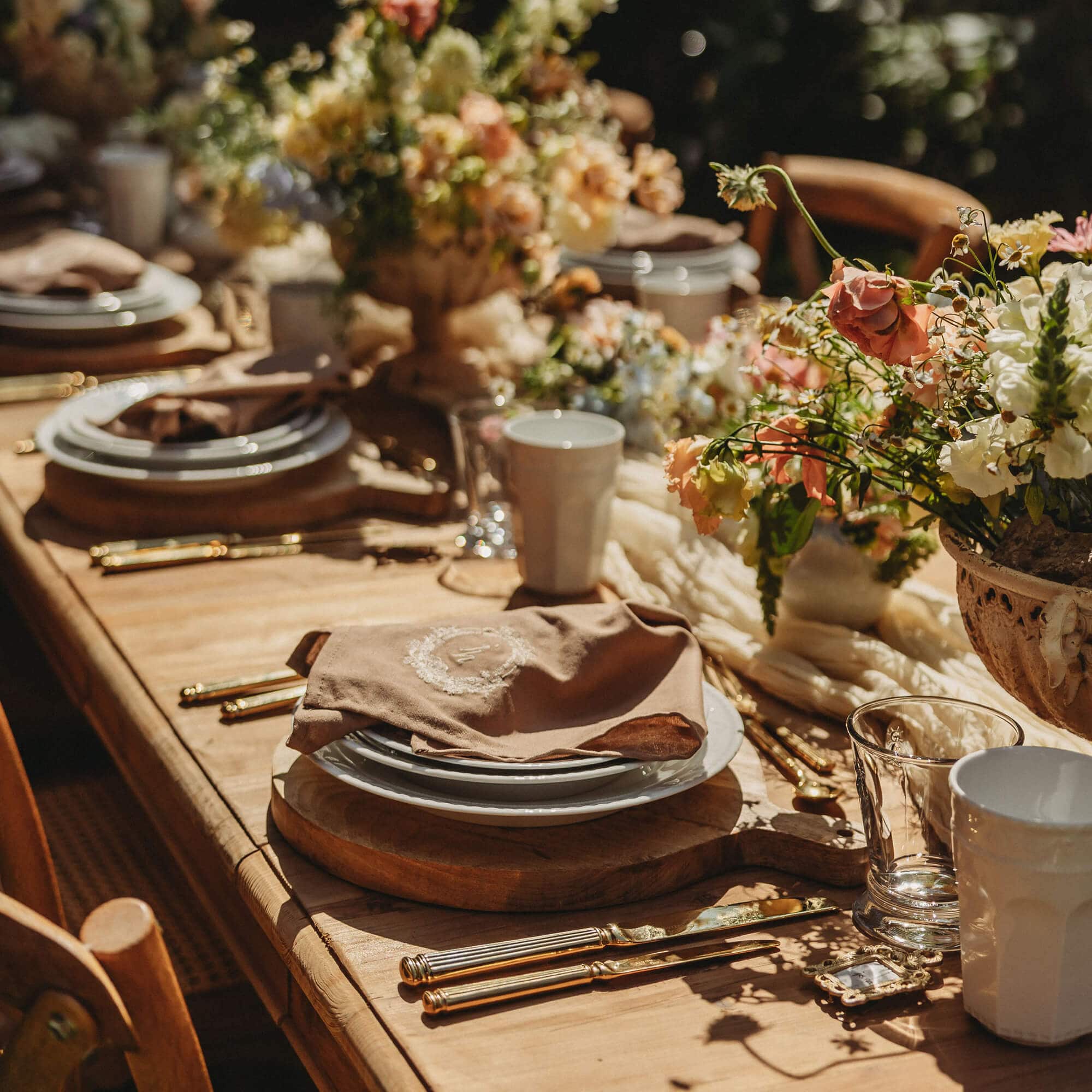 Table en bois rustique dressée avec vaisselle, couverts dorés et décoration florale pour réception