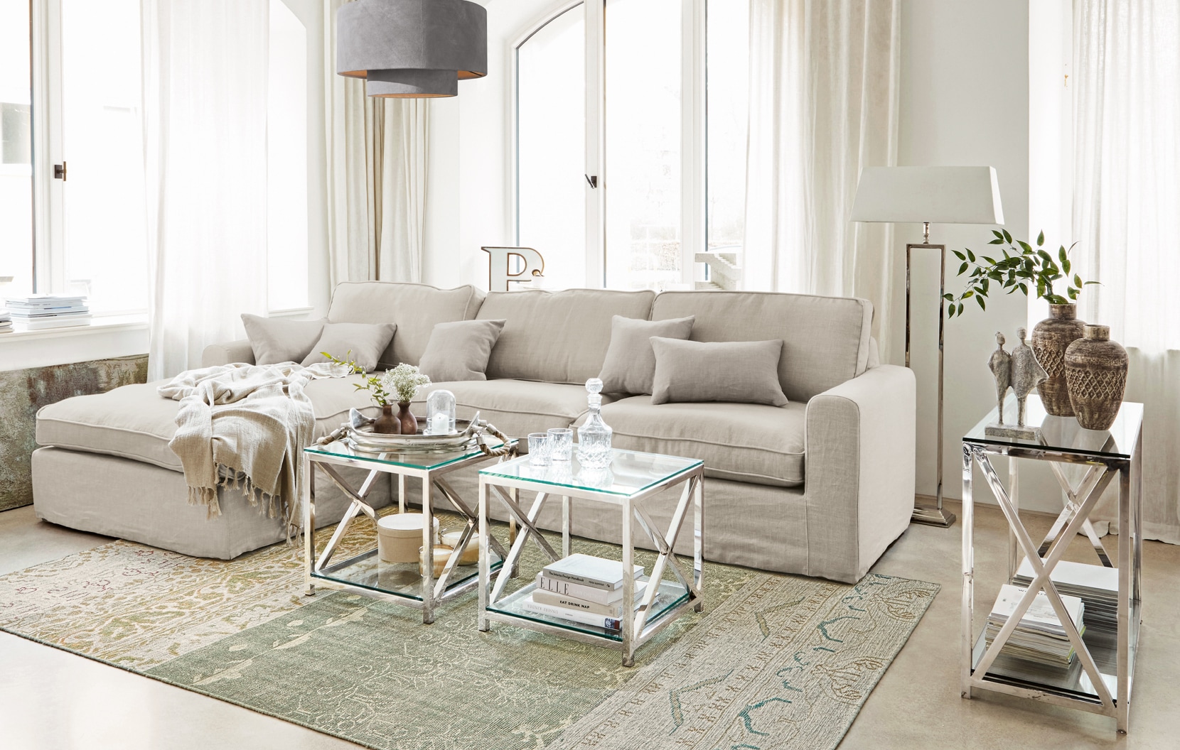 Canapé classique beige en lin avec coussins et tables basses en verre sur cadre métallique dans un salon lumineux