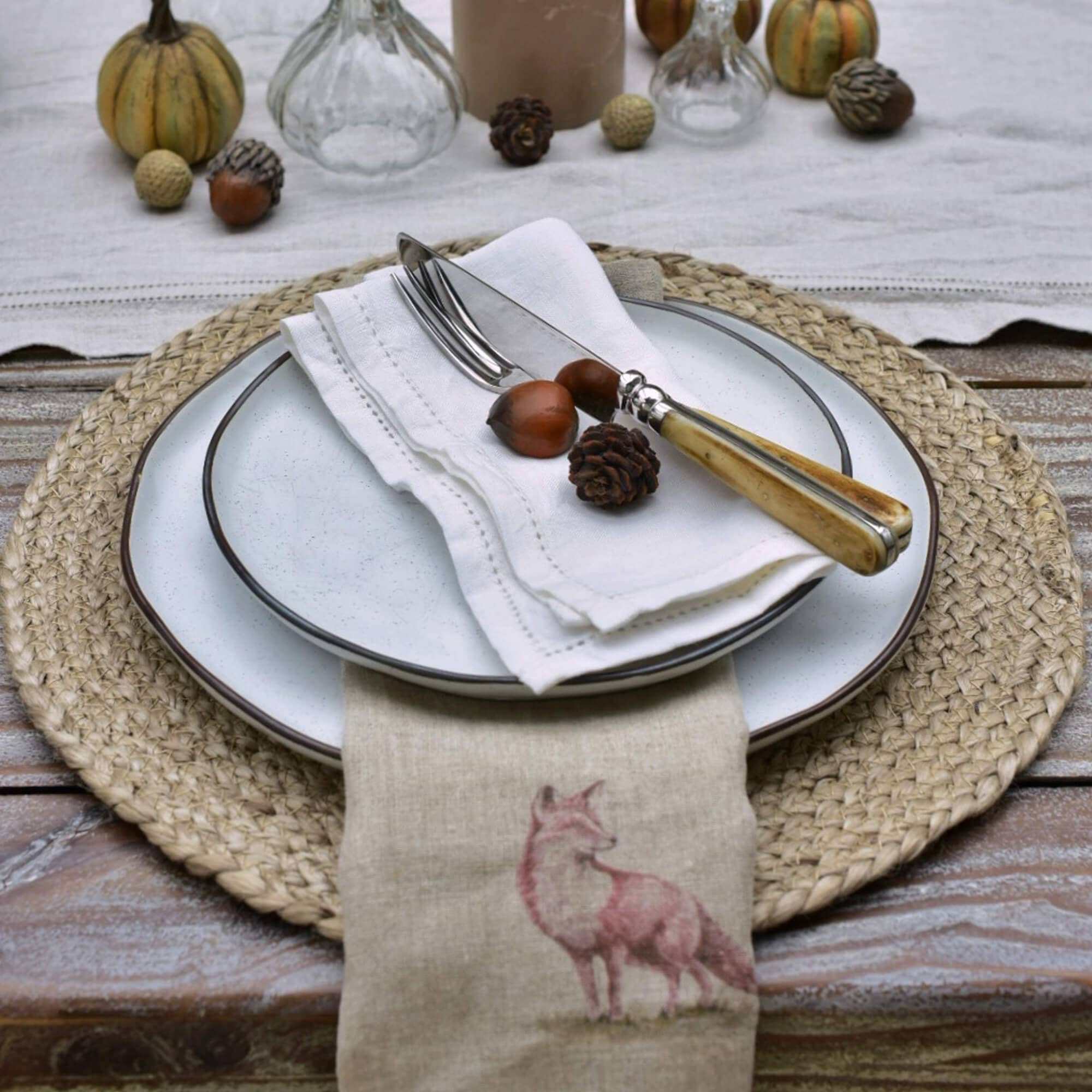 Service de table en céramique blanche avec couverts à manches en bois clair et serviette en lin imprimée d’un renard