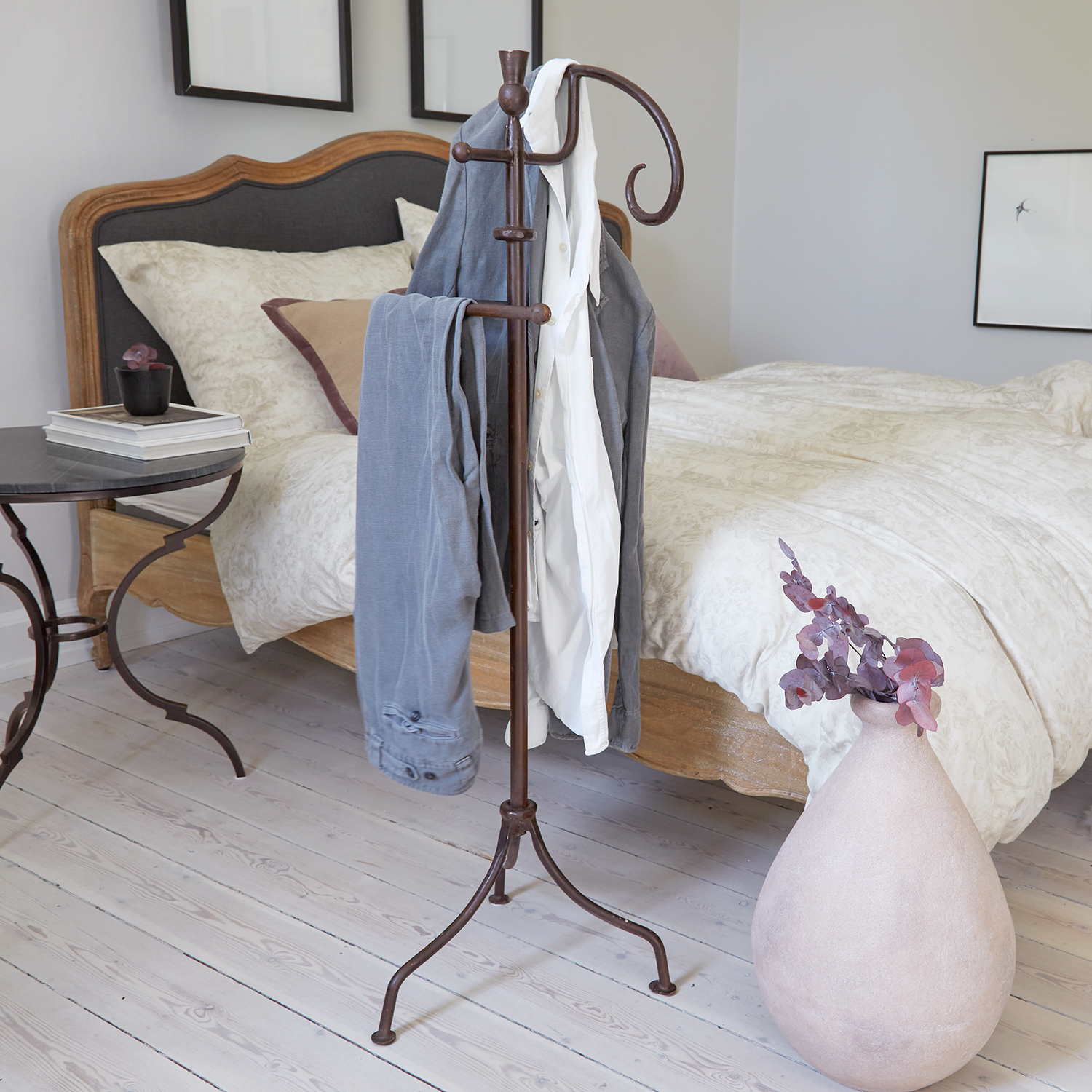 Porte-vêtements en métal style vintage dans une chambre avec lit en bois et literie claire
