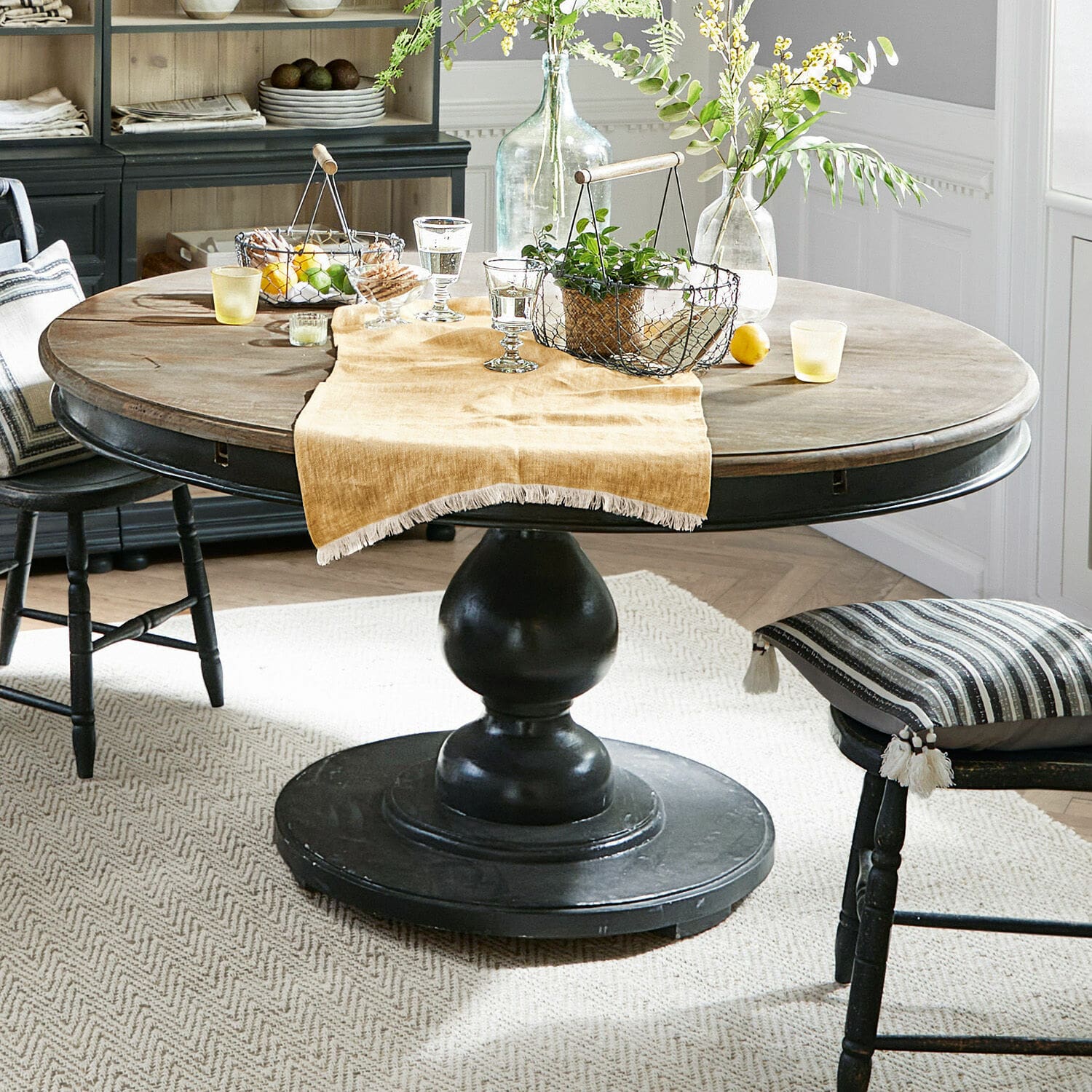 Table Shrewsbury Table ronde en bois avec pied noir et décorations sur nappe beige dans une salle à manger