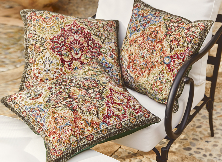 Trois coussins décoratifs avec motif oriental aux couleurs chaudes sur un fauteuil blanc en métal