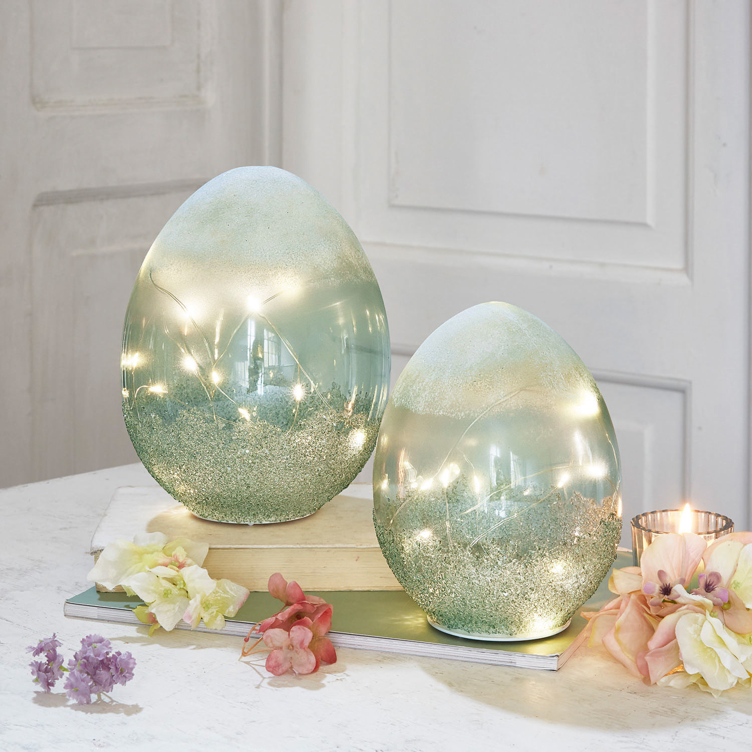 Lot de 2 œufs à LED Borleos Œufs décoratifs en verre vert avec lumières LED intégrées sur une table avec fleurs et bougie