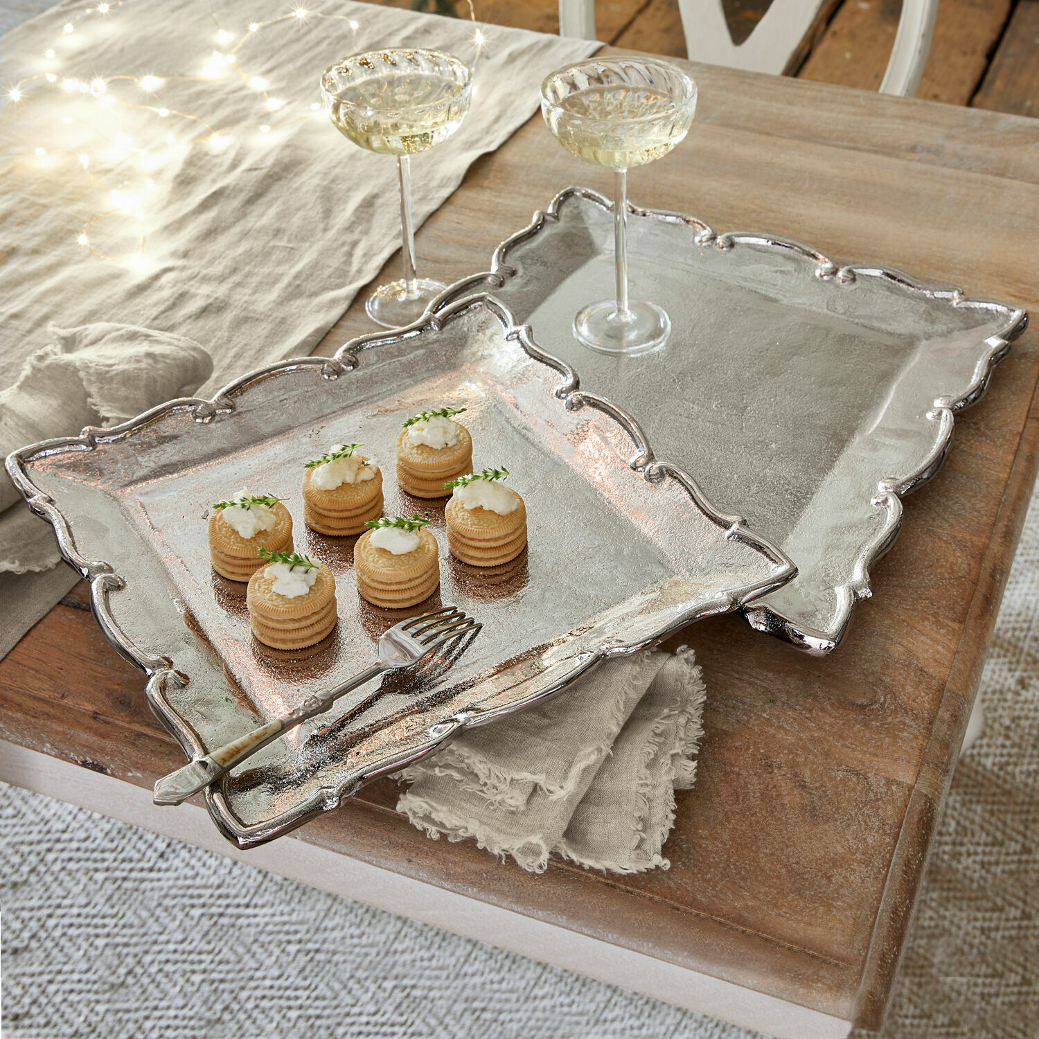 Lot de 2 plateaux Trevor Deux plateaux en métal argenté avec bord décoratif sur table en bois avec amuse-bouches et verres à vin