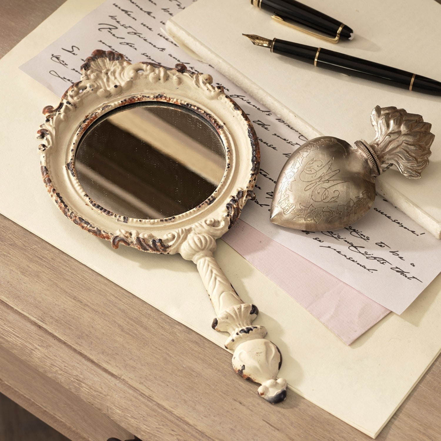 Miroir portatif Empuré Miroir à main décoratif en métal vieilli crème posé sur une table en bois avec stylo plume et lettres