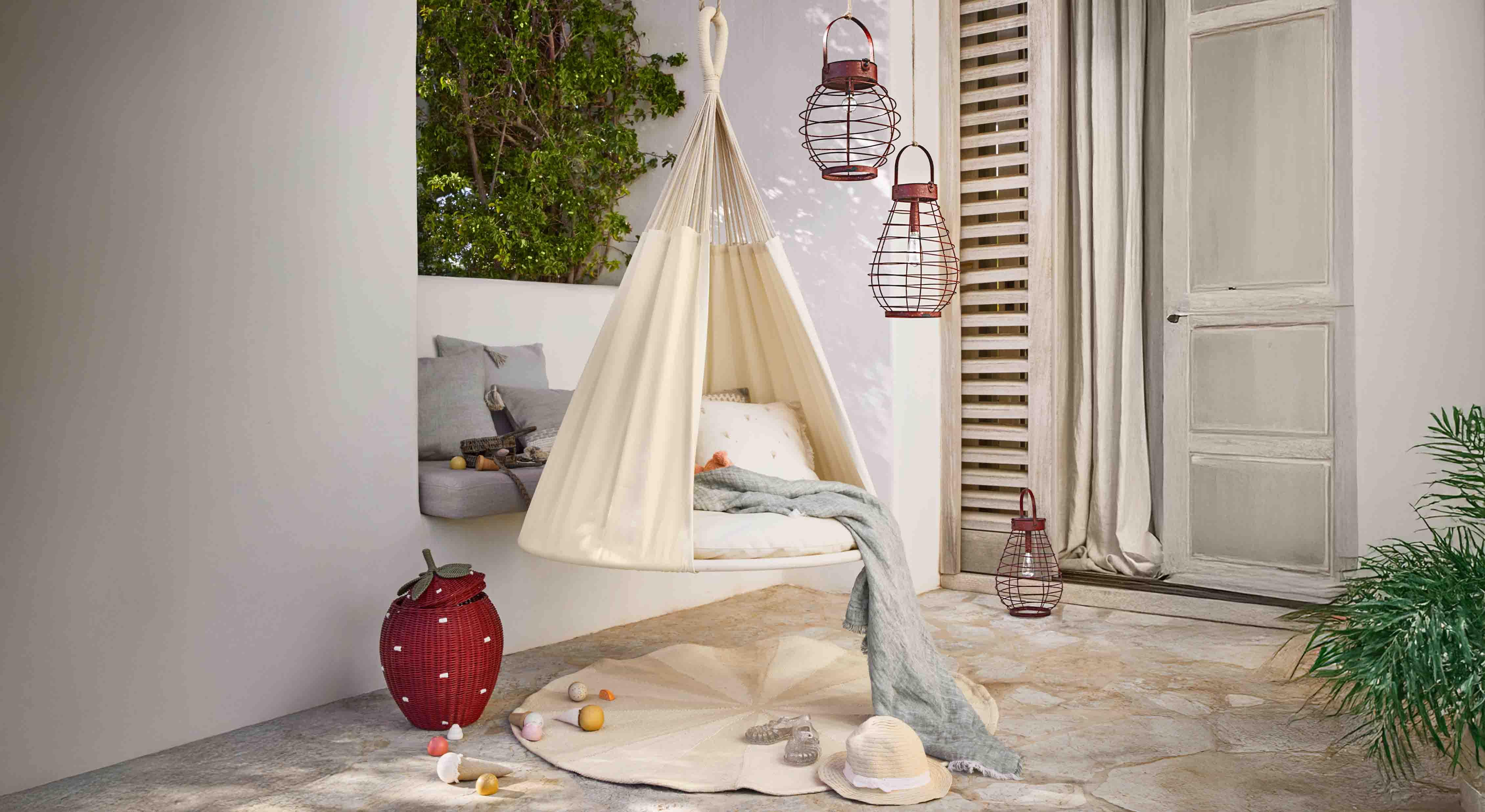 Fauteuil suspendu beige en tissu sur terrasse avec coussins et lanternes décoratives en métal