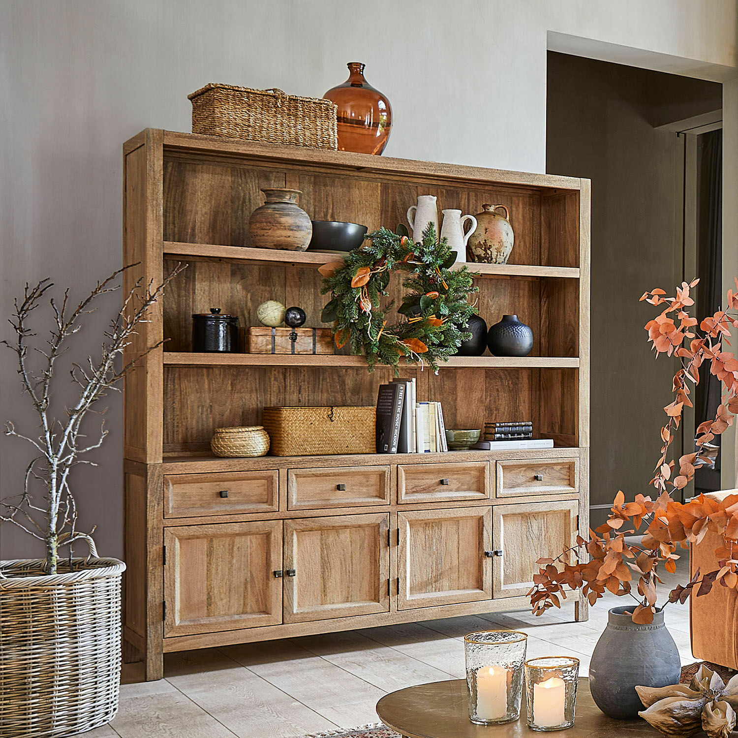 Vaisselier New Bedford Buffet en bois naturel avec étagères et tiroirs décoré de vases, livres et bougies dans un salon