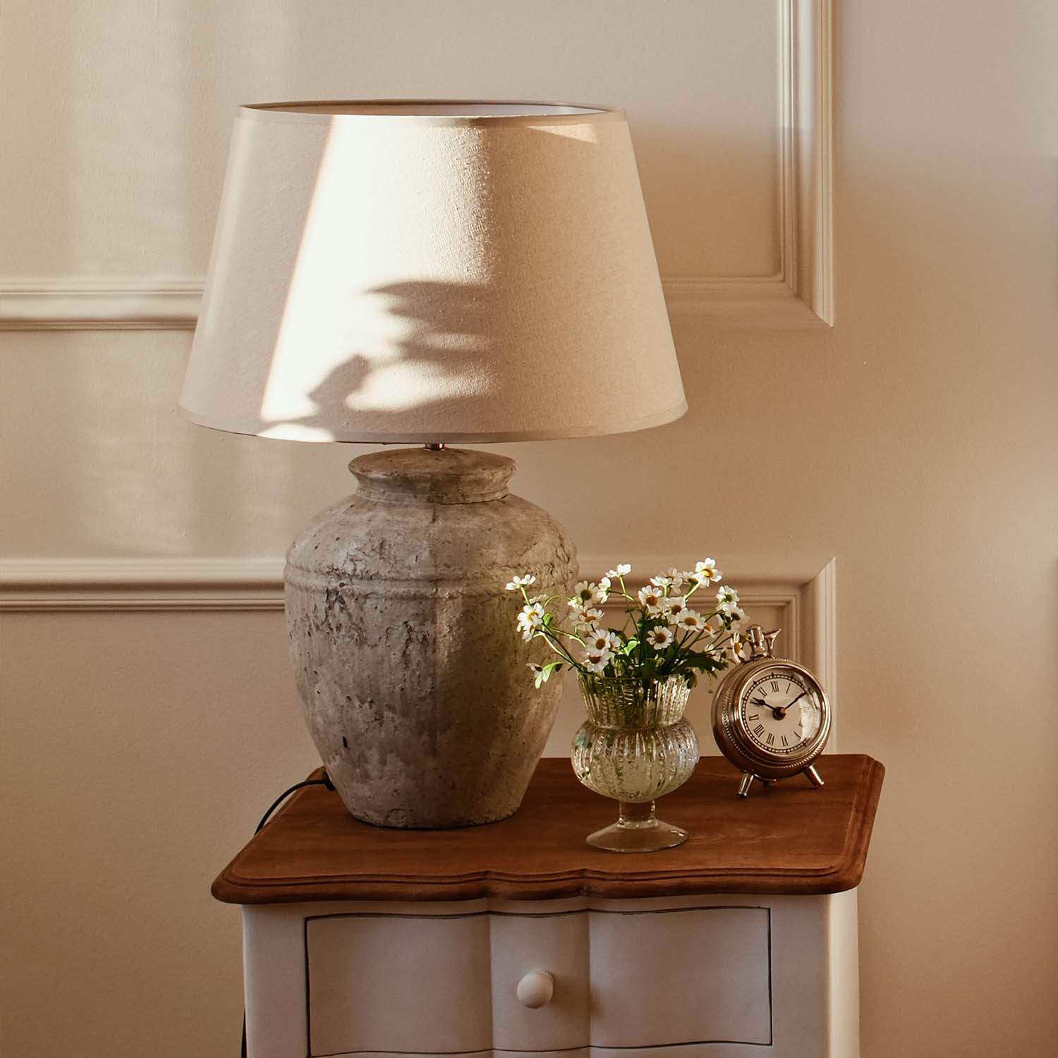 Lampe de table avec abat-jour beige et base en céramique vintage sur table en bois avec fleurs et horloge