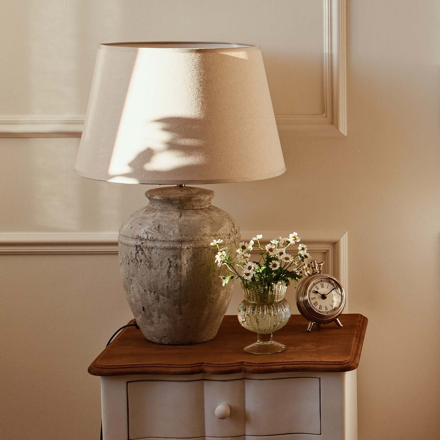 Lampe de table avec abat-jour beige et base en céramique vintage sur table en bois avec fleurs et horloge