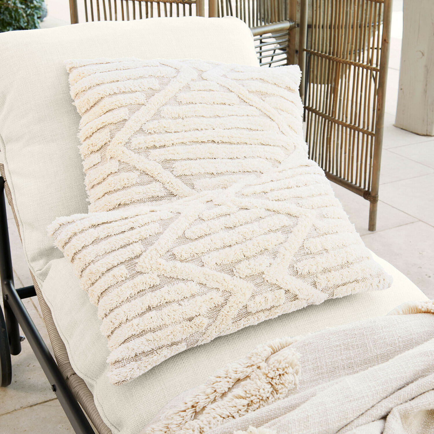 Deux coussins décoratifs crème en tissu doux avec motif géométrique sur un transat clair