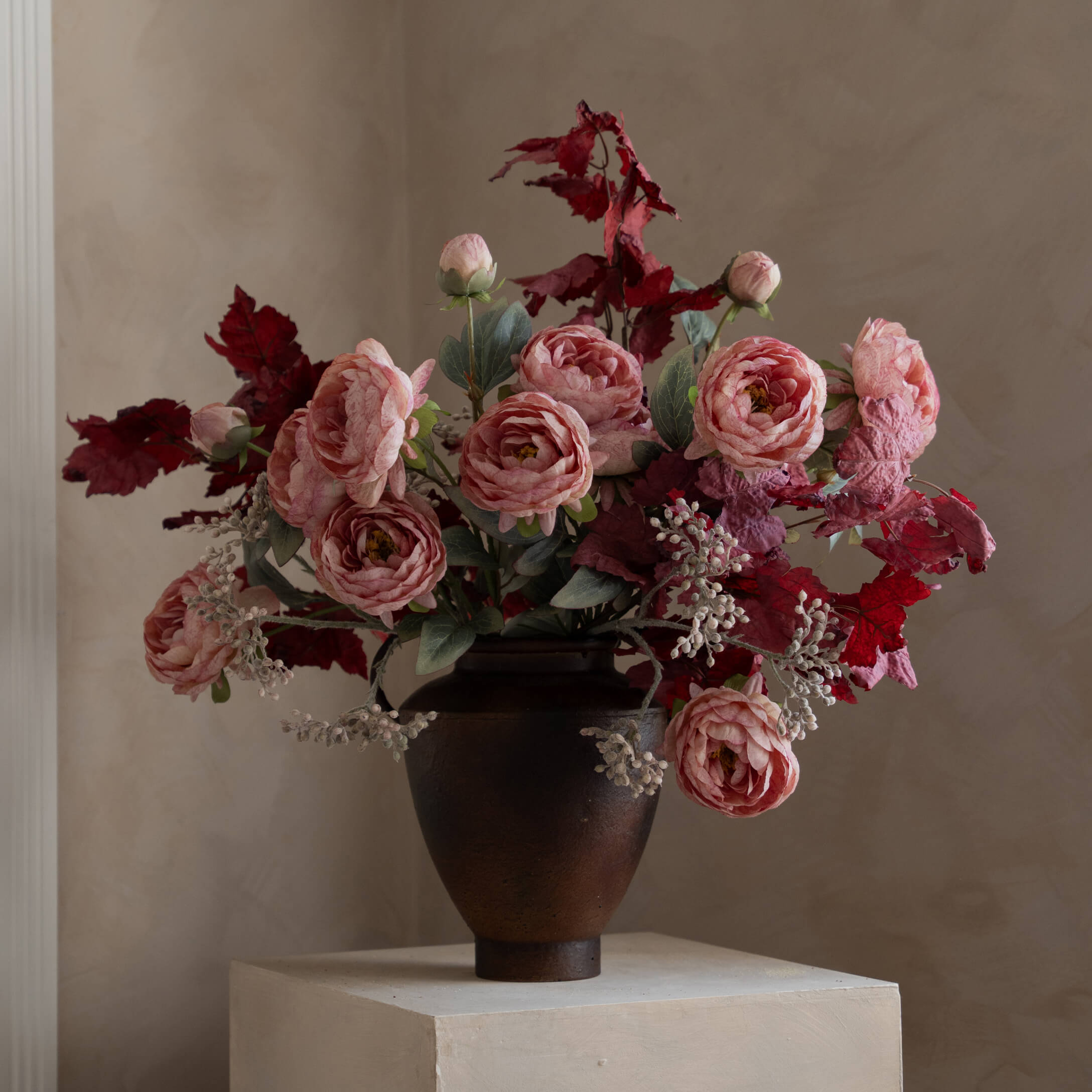 Bouquet de roses roses et feuilles rouges dans un vase en céramique foncé sur un socle clair