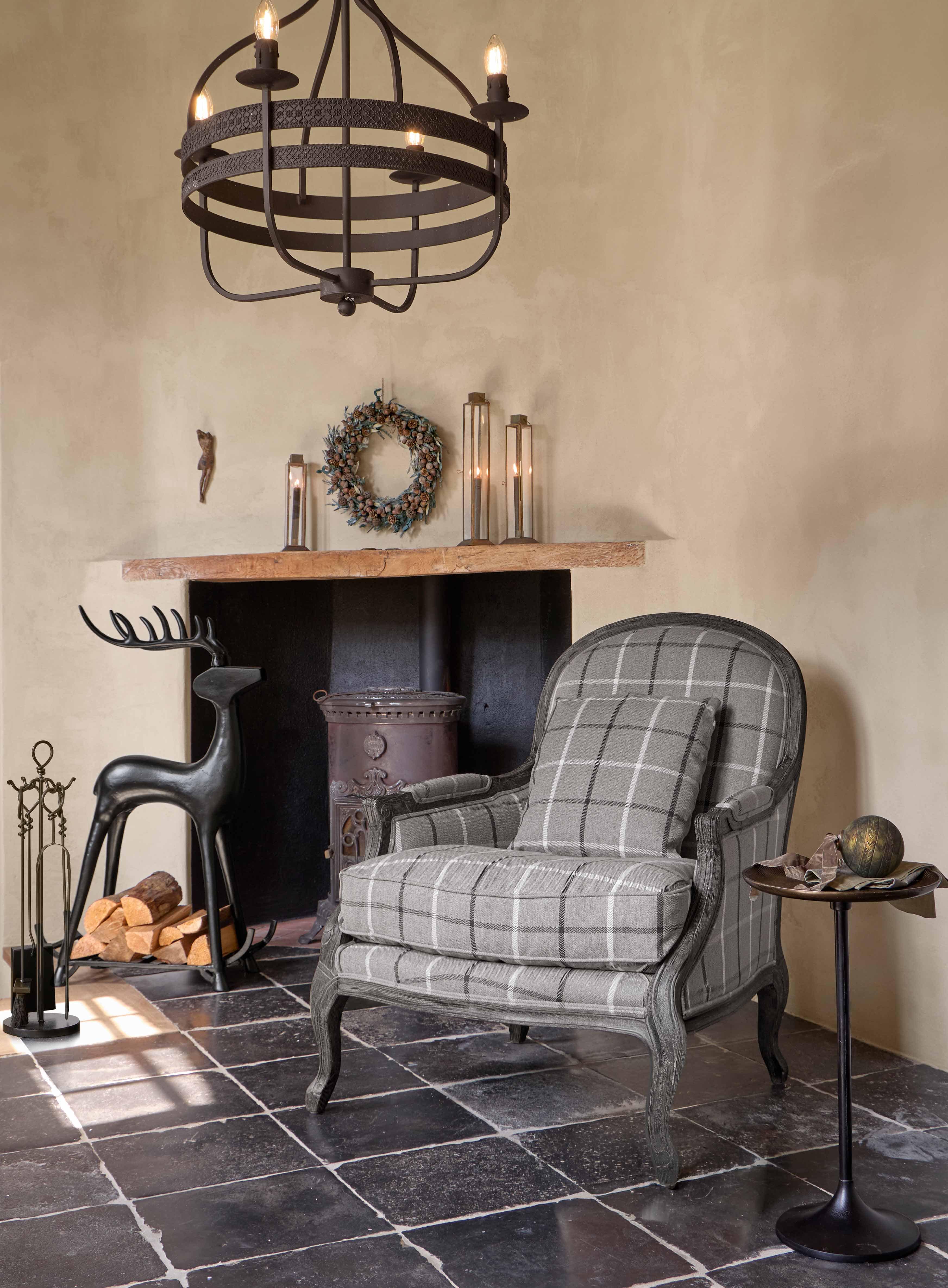 Fauteuil gris à carreaux avec cadre en bois dans un salon chaleureux avec cheminée et décoration rustique