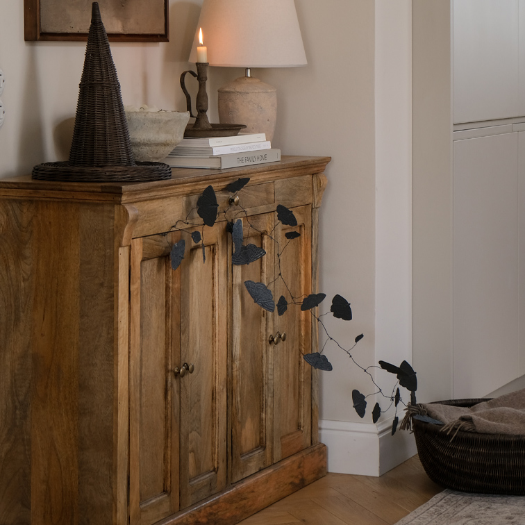 Buffet en bois avec guirlande de feuilles noires et lampe de table dans un intérieur chaleureux