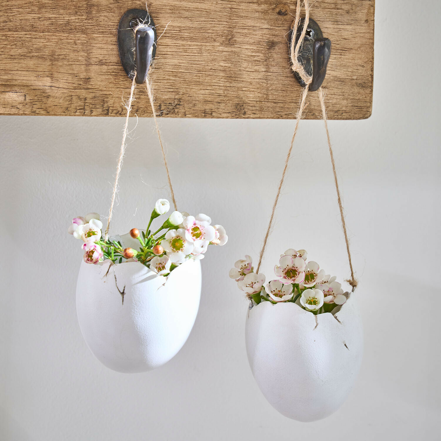 Lot de 2 vases à suspendre Nalena Deux pots suspendus en forme d'œufs blancs en céramique avec des fleurs, accrochés à une planche en bois