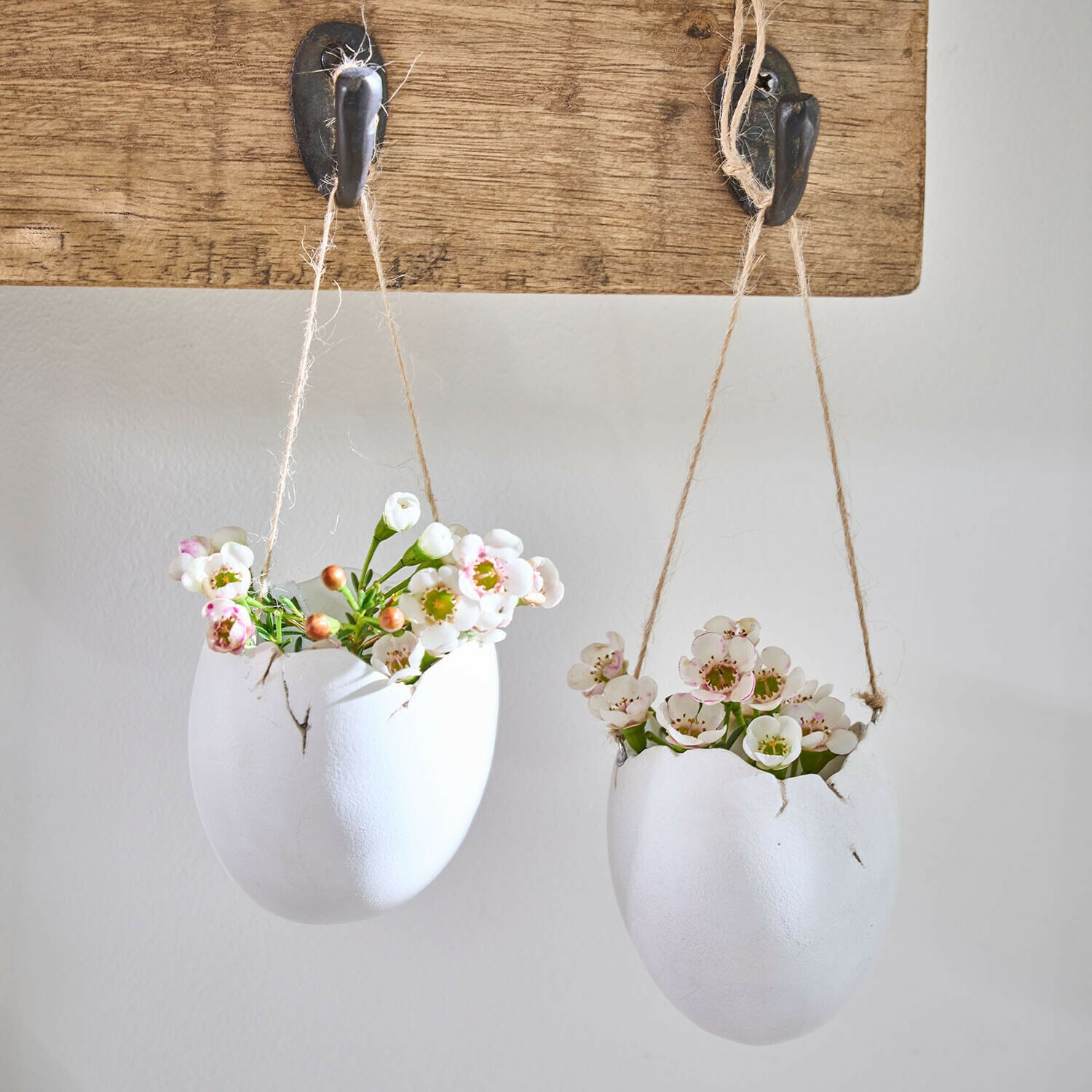 Lot de 2 vases à suspendre Nalena Deux pots suspendus en forme d'œufs blancs en céramique avec des fleurs, accrochés à une planche en bois