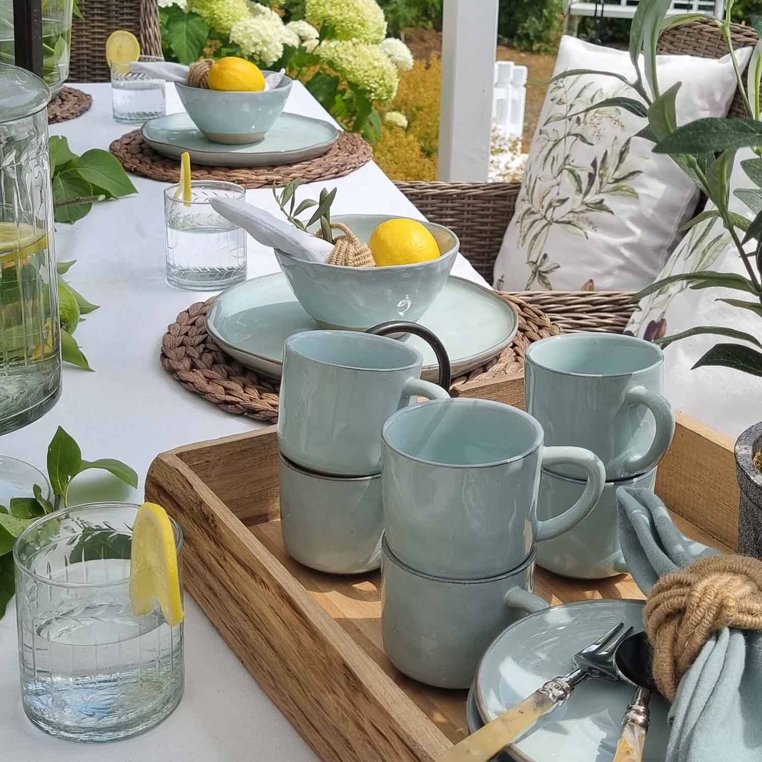 Service de vaisselle en céramique bleu clair sur plateau en bois avec citrons et verres d'eau