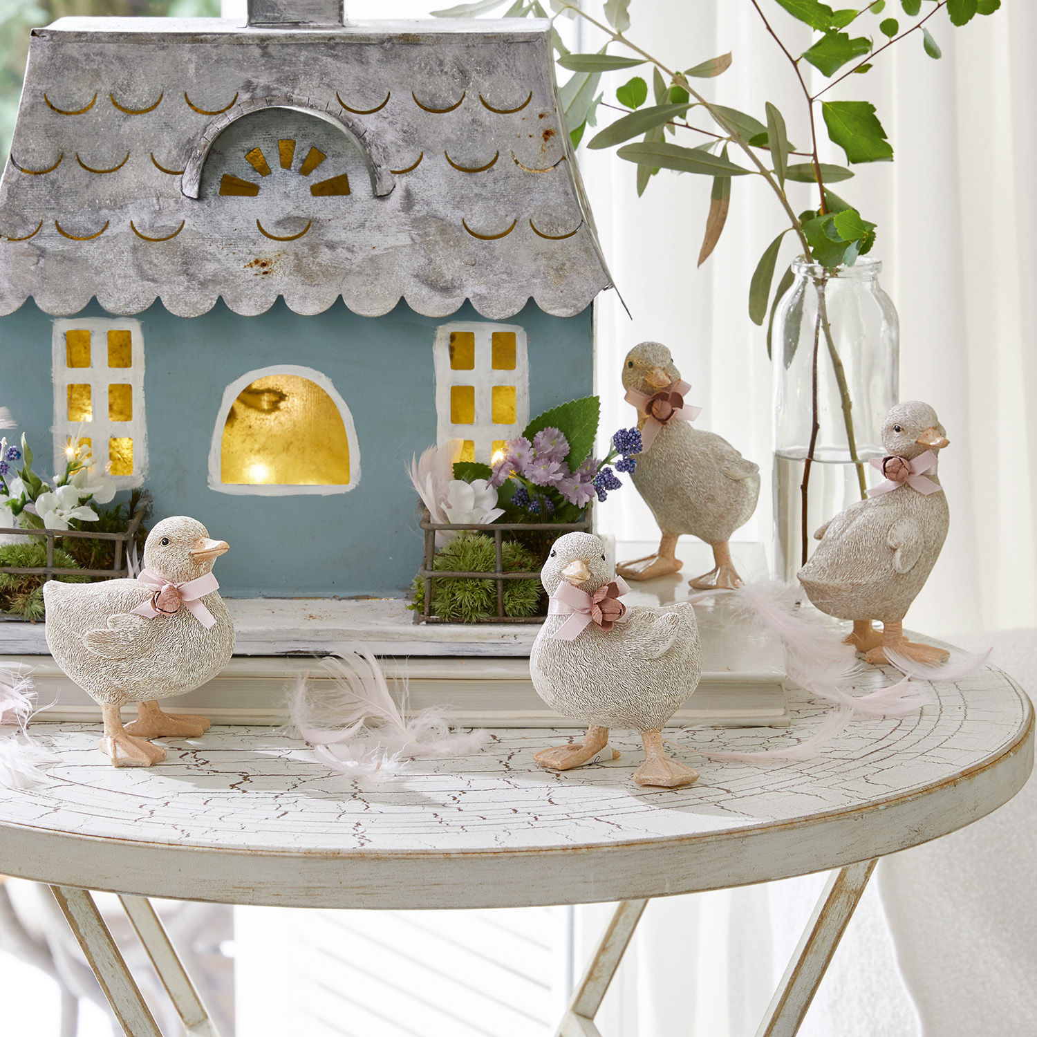 Lot de 4 canetons Orélie Figurines décoratives de canards en matériau clair sur une table blanche avec maison et fleurs