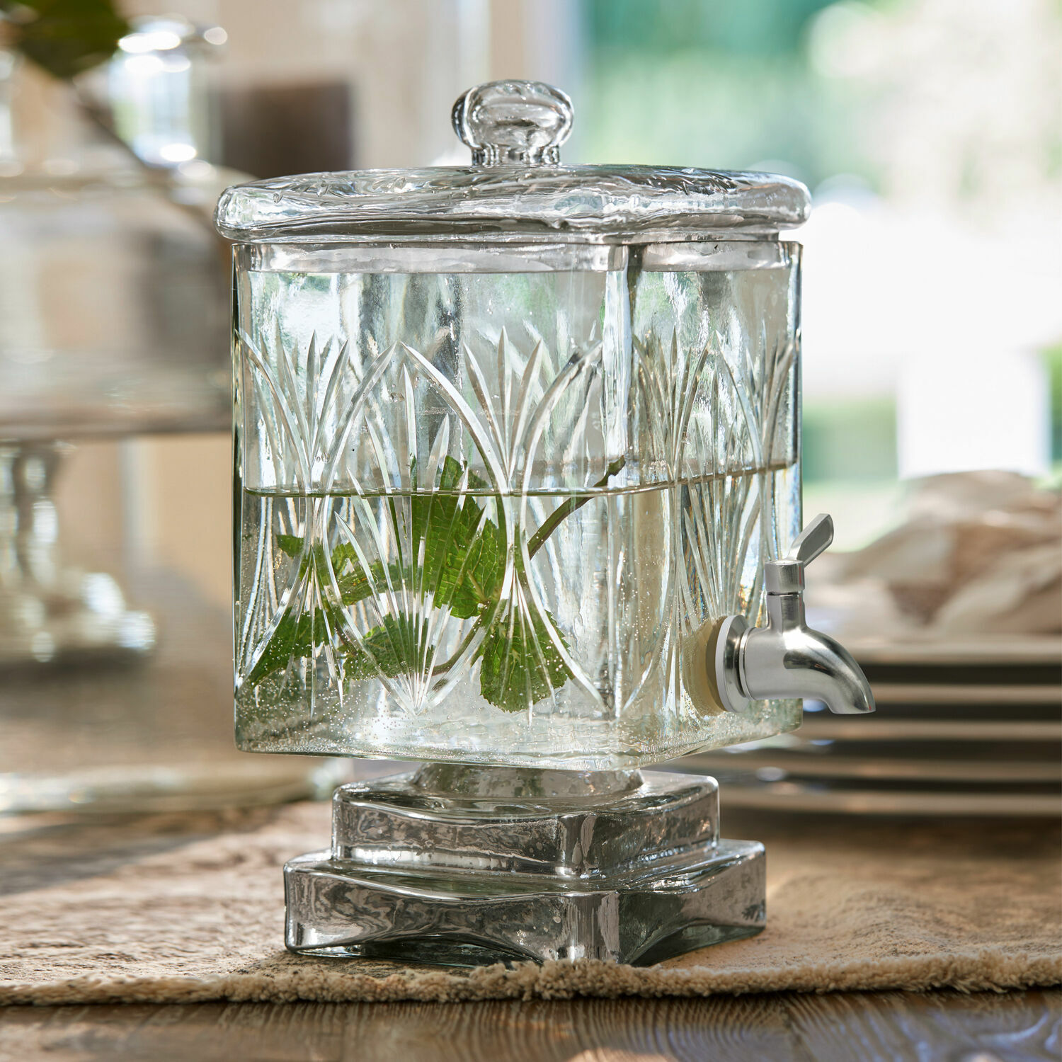 Distributeur de boisson Logan Distributeur de boissons en verre avec couvercle et robinet, décoré de motifs et feuilles vertes.
