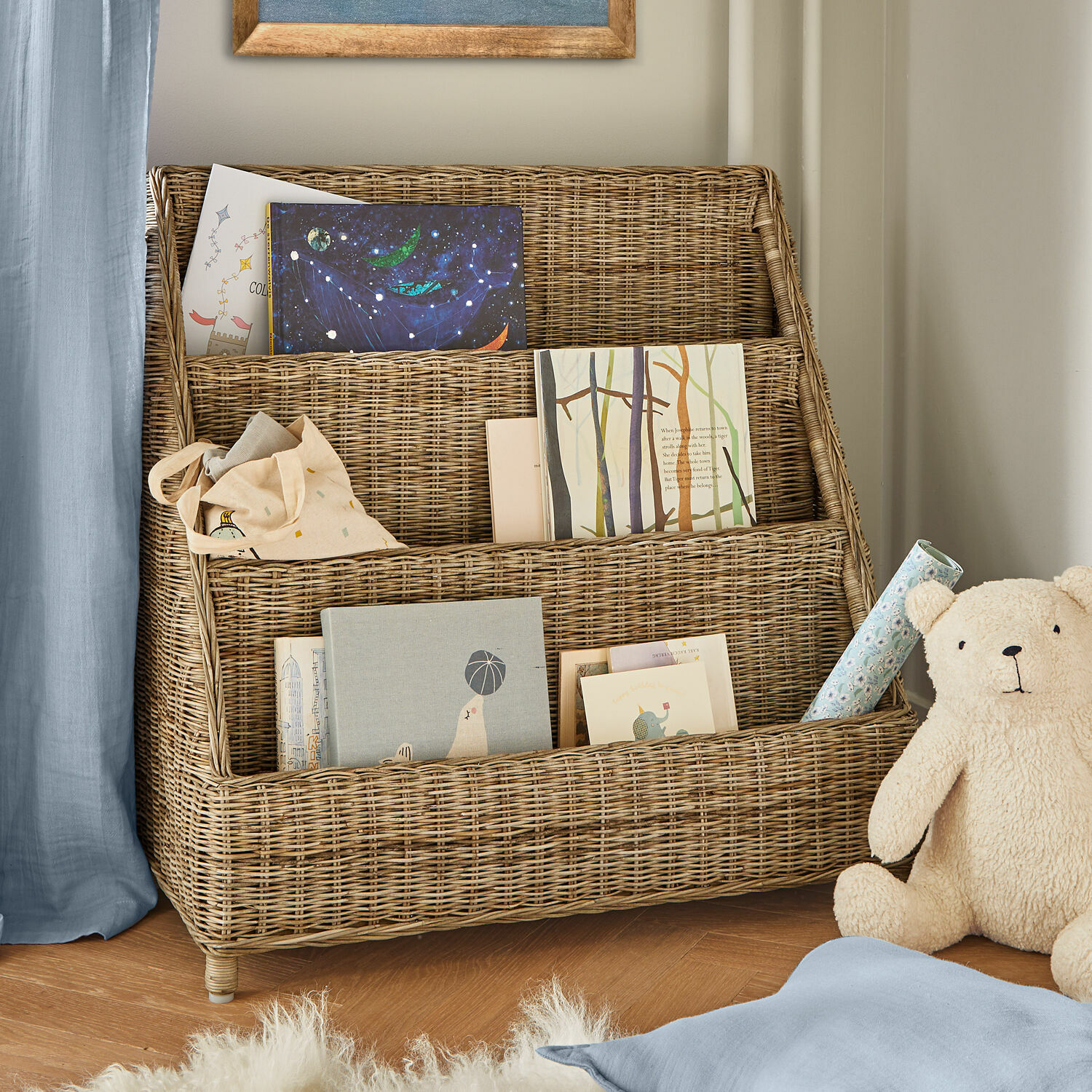 Bibliothèque Trésolia Étagère à trois niveaux en rotin naturel avec livres et ours en peluche dans une chambre d'enfant
