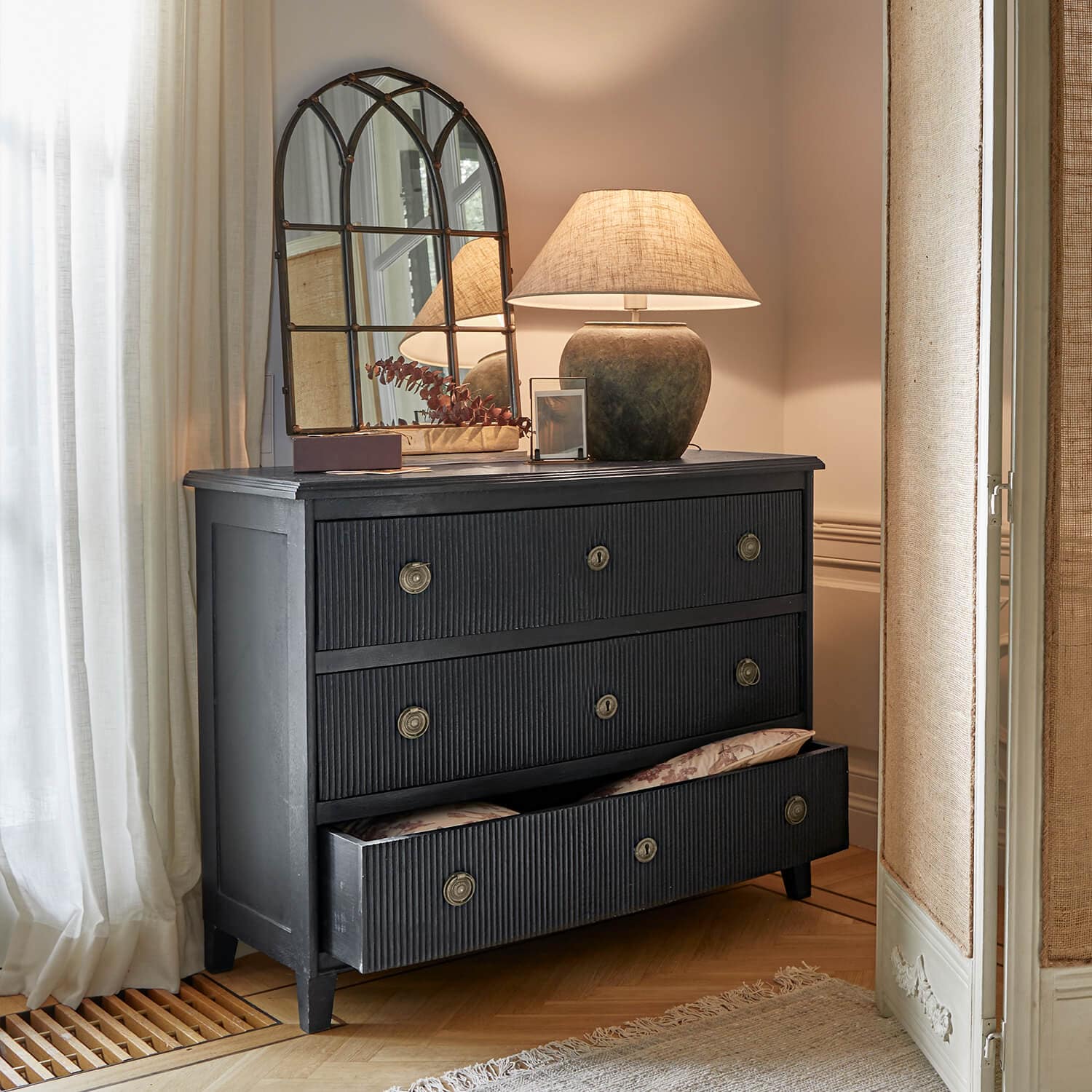 Commode noire en bois avec trois tiroirs et poignées en métal dans un intérieur classique