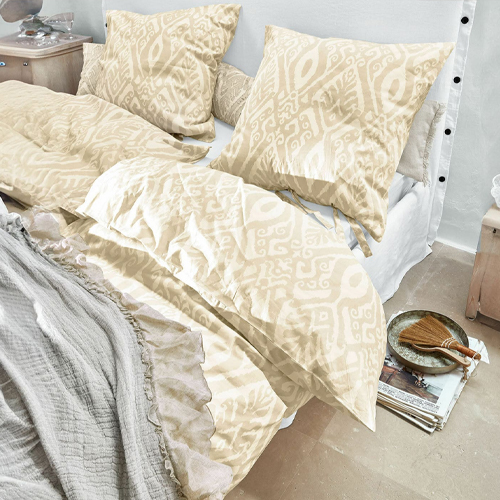 Parure de lit beige à motifs géométriques en tissu doux sur un lit dans une chambre lumineuse