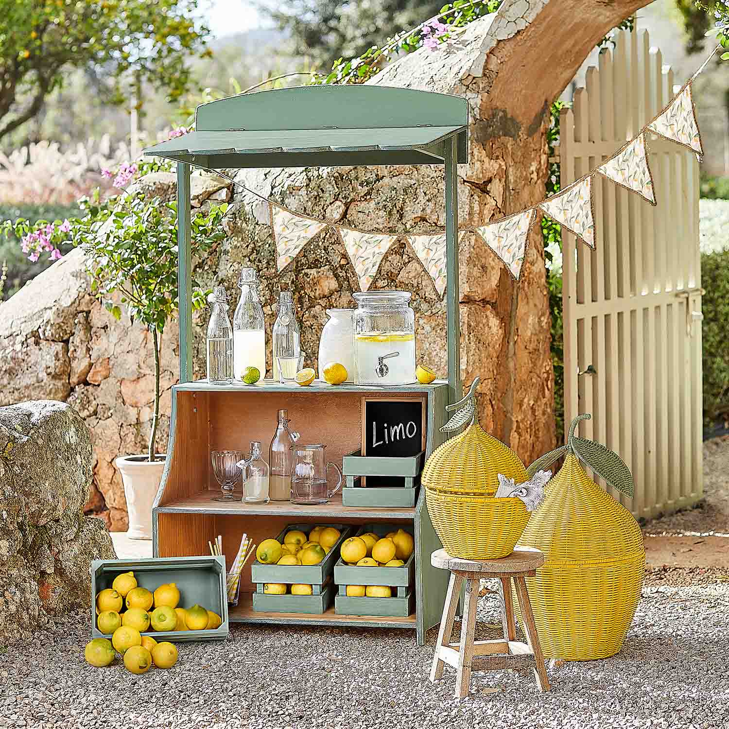 Étal en bois vert avec citrons et bouteilles en verre pour limonade dans un jardin ensoleillé