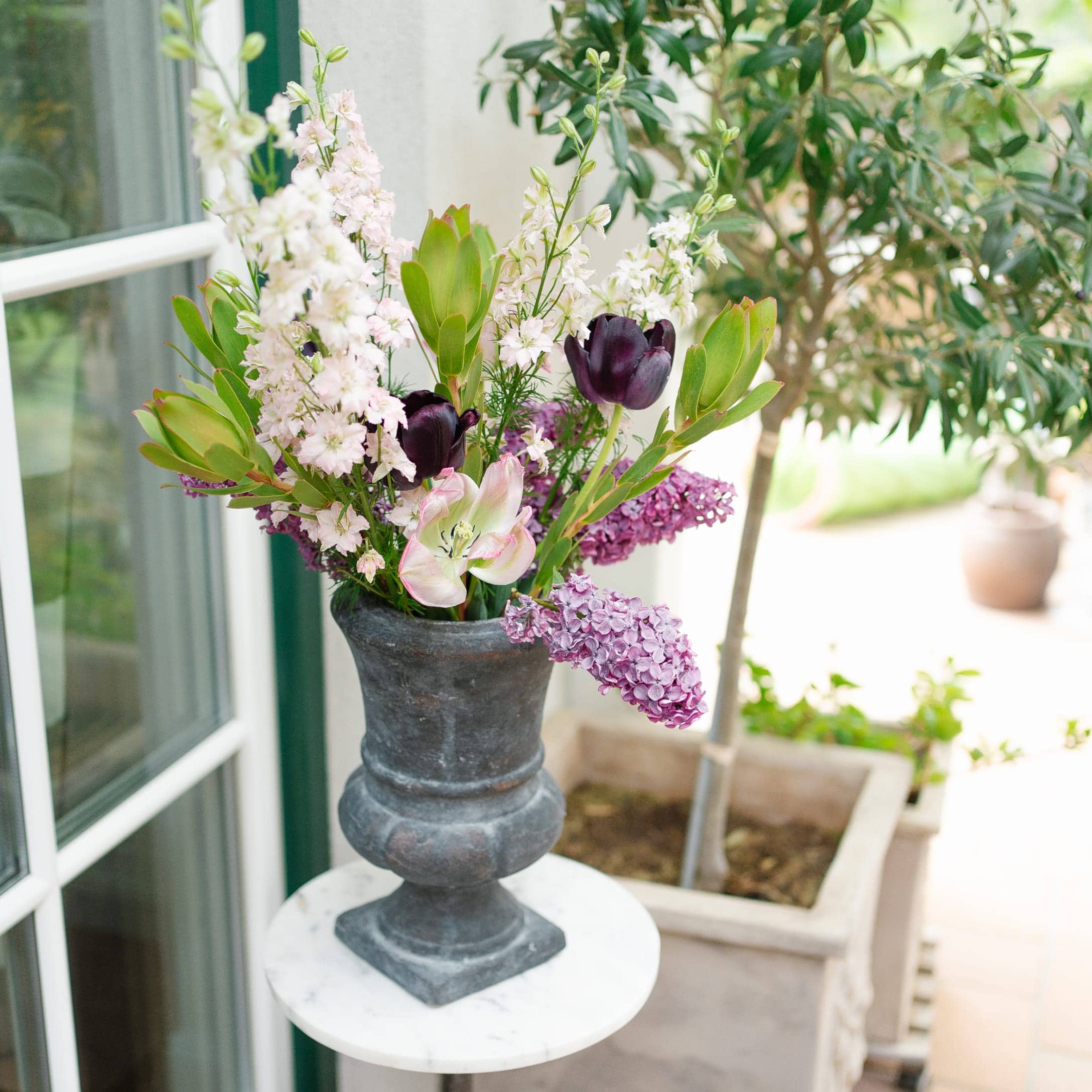 Vase décoratif en pierre grise foncée avec bouquet de fleurs roses et violettes sur une table ronde