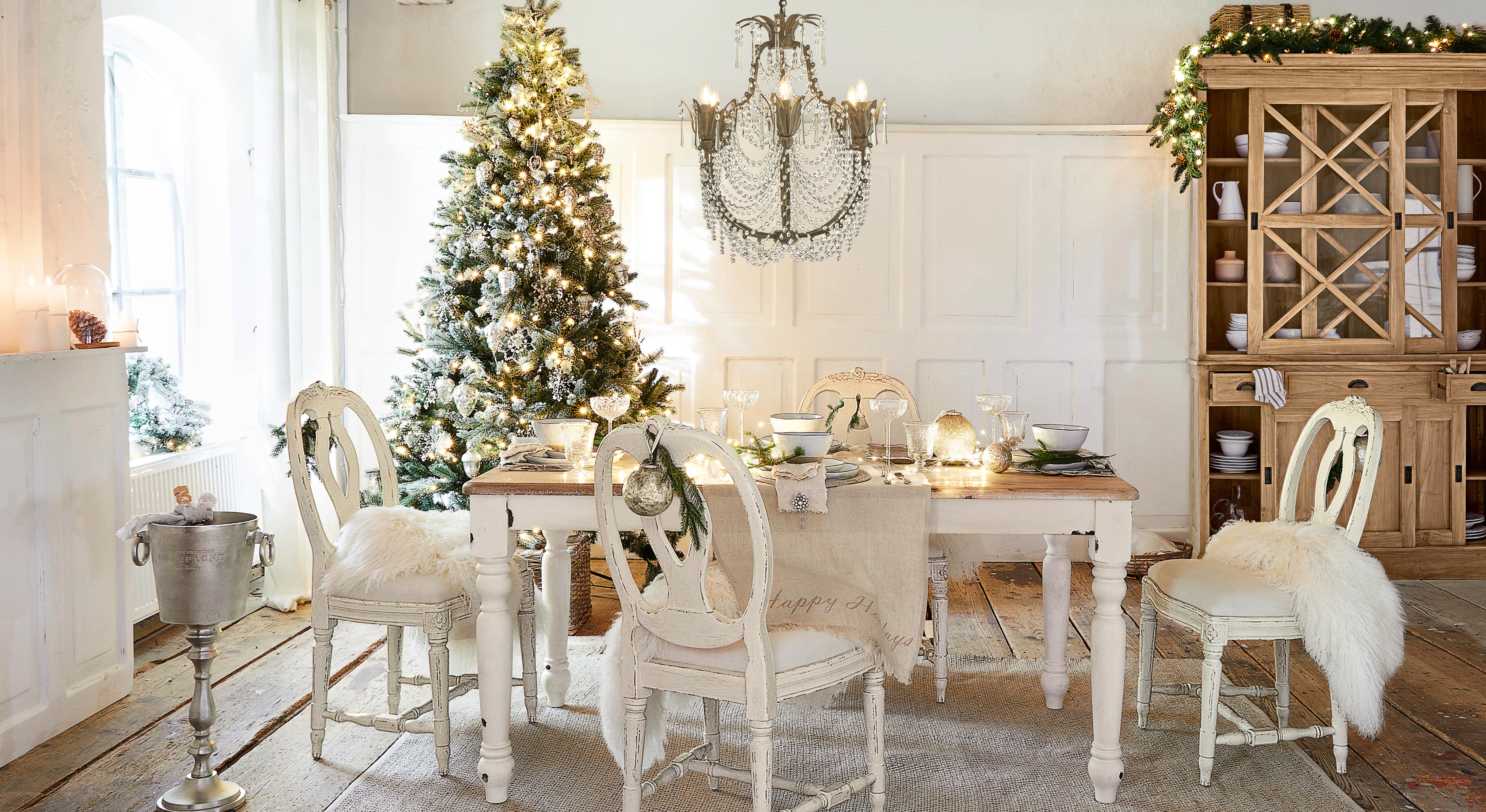Salle à manger avec table et chaises blanches en bois, décorée pour Noël avec sapin et lustre en cristal