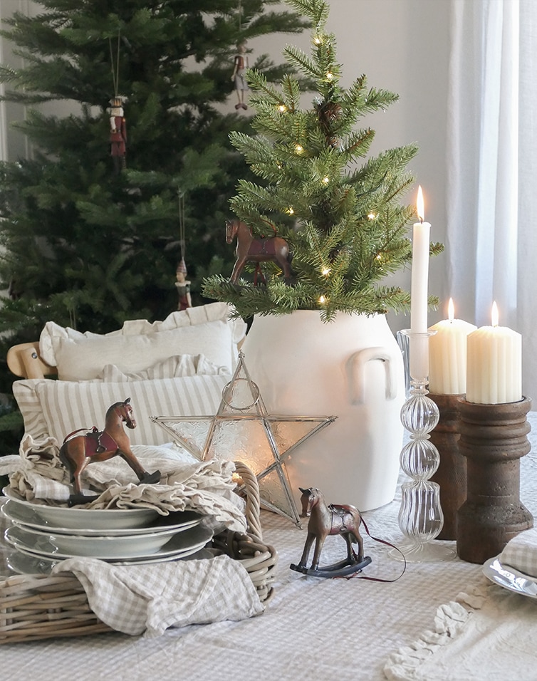 Décoration de Noël avec pichet blanc, sapin vert, bougies et chevaux à bascule en bois sur table