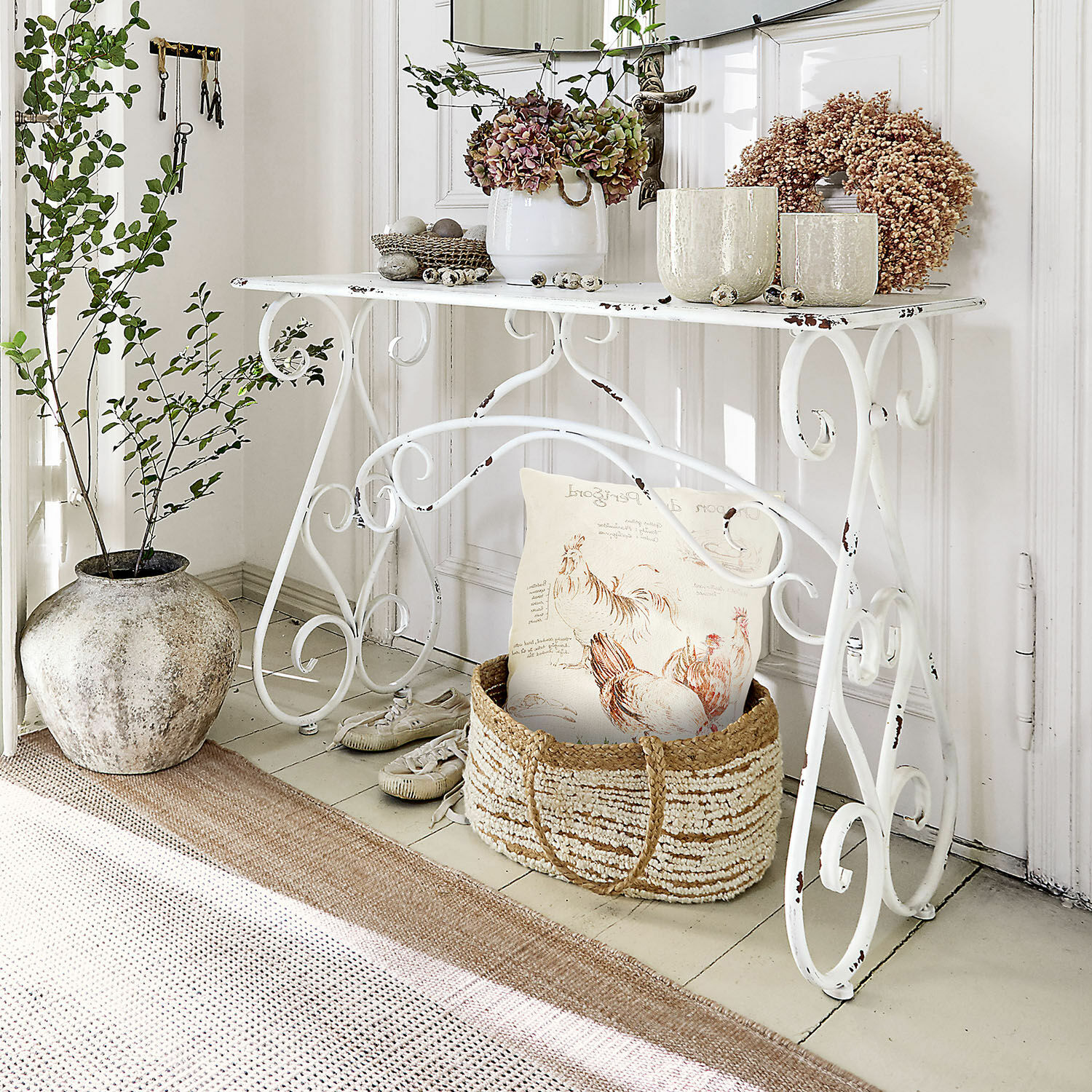 Console Stonem Table en métal blanc avec plantes décoratives et panier en osier avec coussin dans un style rustique