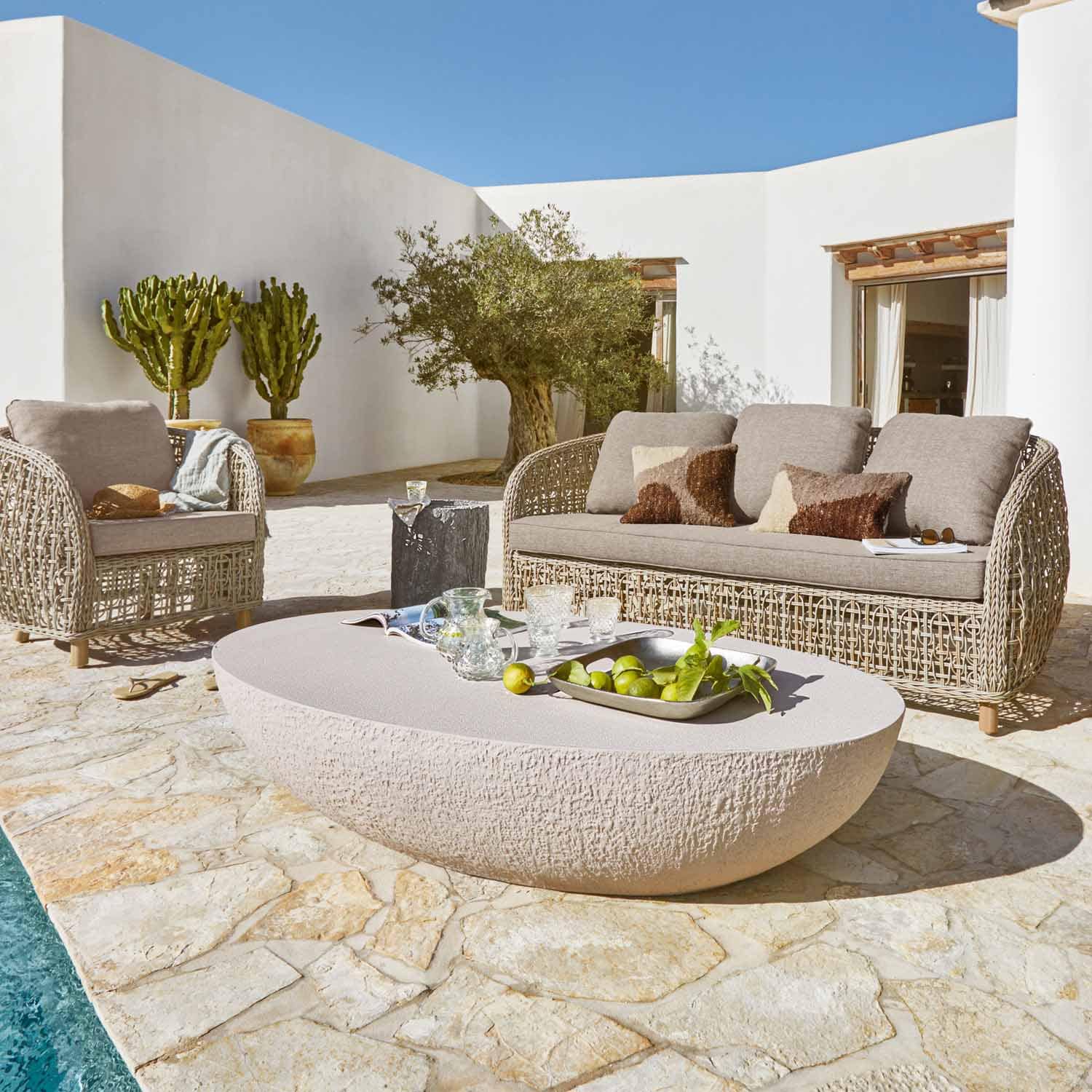 Ensemble de mobilier de jardin en rotin beige avec coussins et table en pierre sur terrasse près de la piscine
