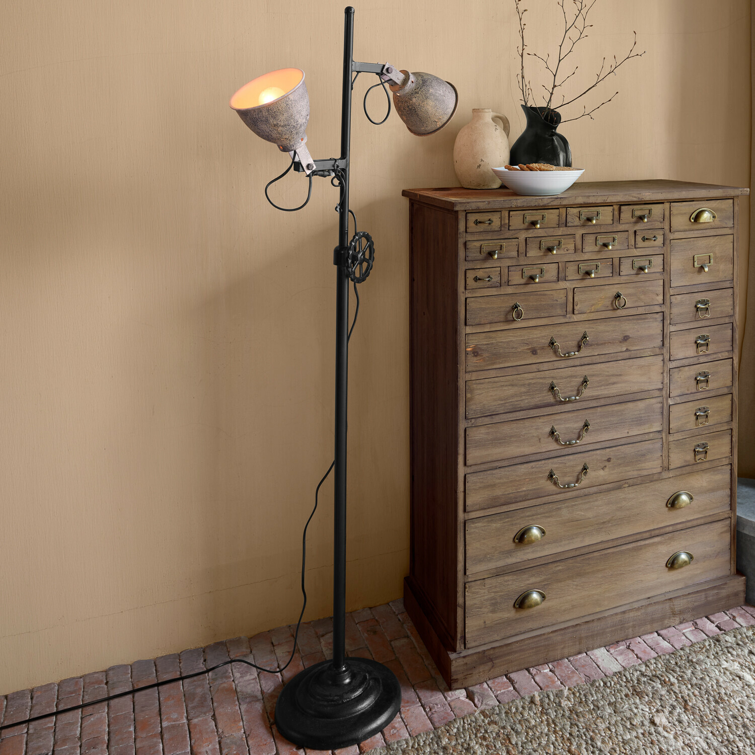 Lampadaire Fenric Lampadaire en métal noir avec abat-jours gris patinés à côté d'une commode en bois rustique