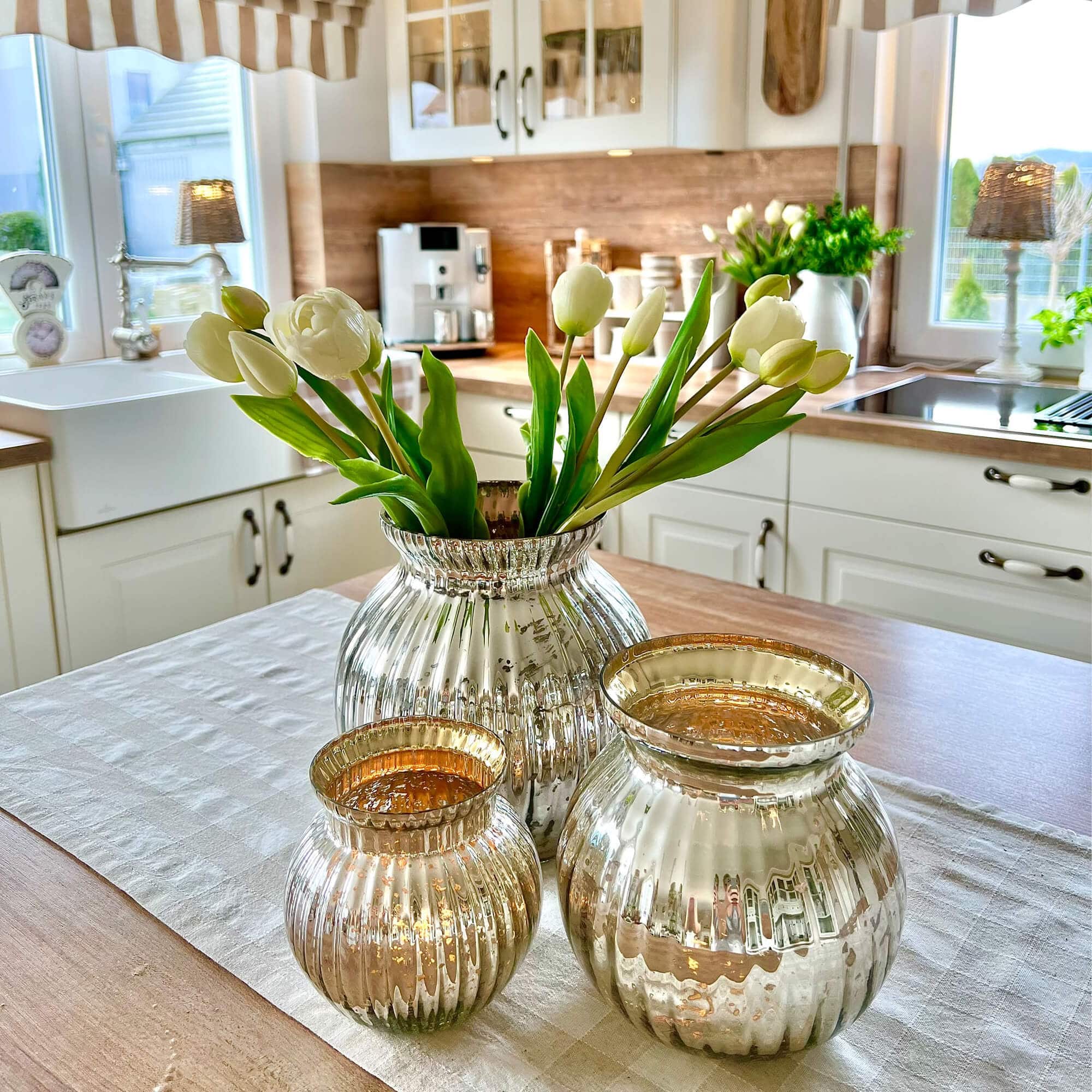 Ensemble de trois vases en verre argenté sur une table en bois dans une cuisine avec tulipes blanches