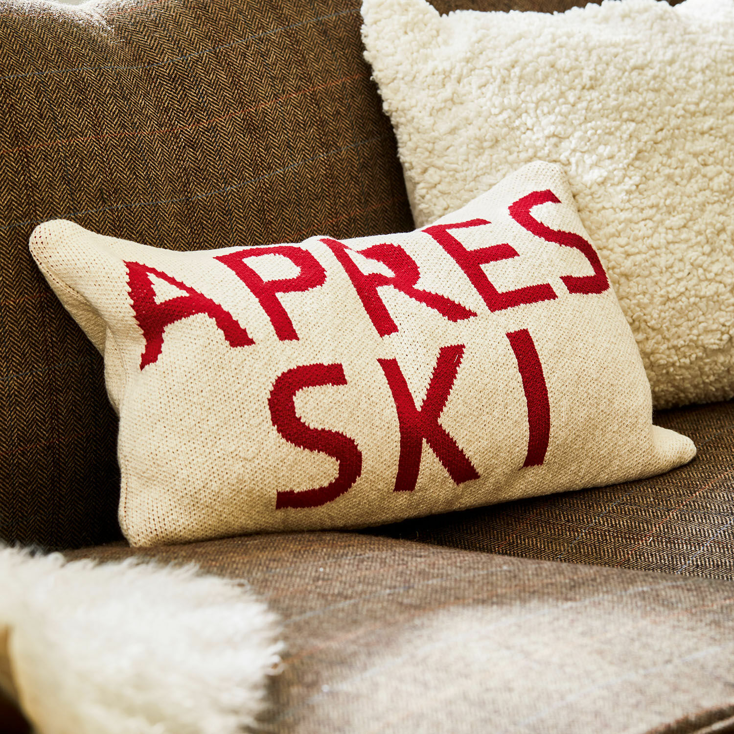 Housse de coussin Apres Ski Coussin beige avec inscription rouge Apres Ski sur canapé marron avec plaid en fausse fourrure