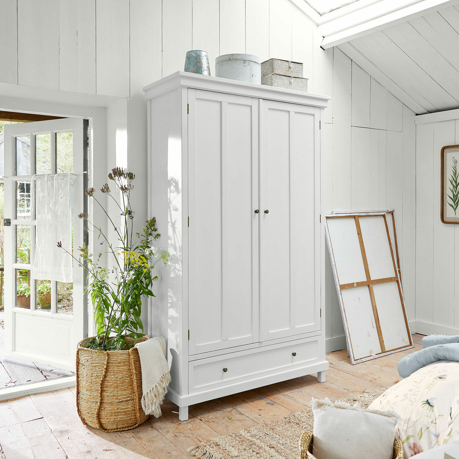 Armoire Sirevol Armoire blanche en bois à deux portes et tiroir dans une pièce lumineuse avec panier en osier