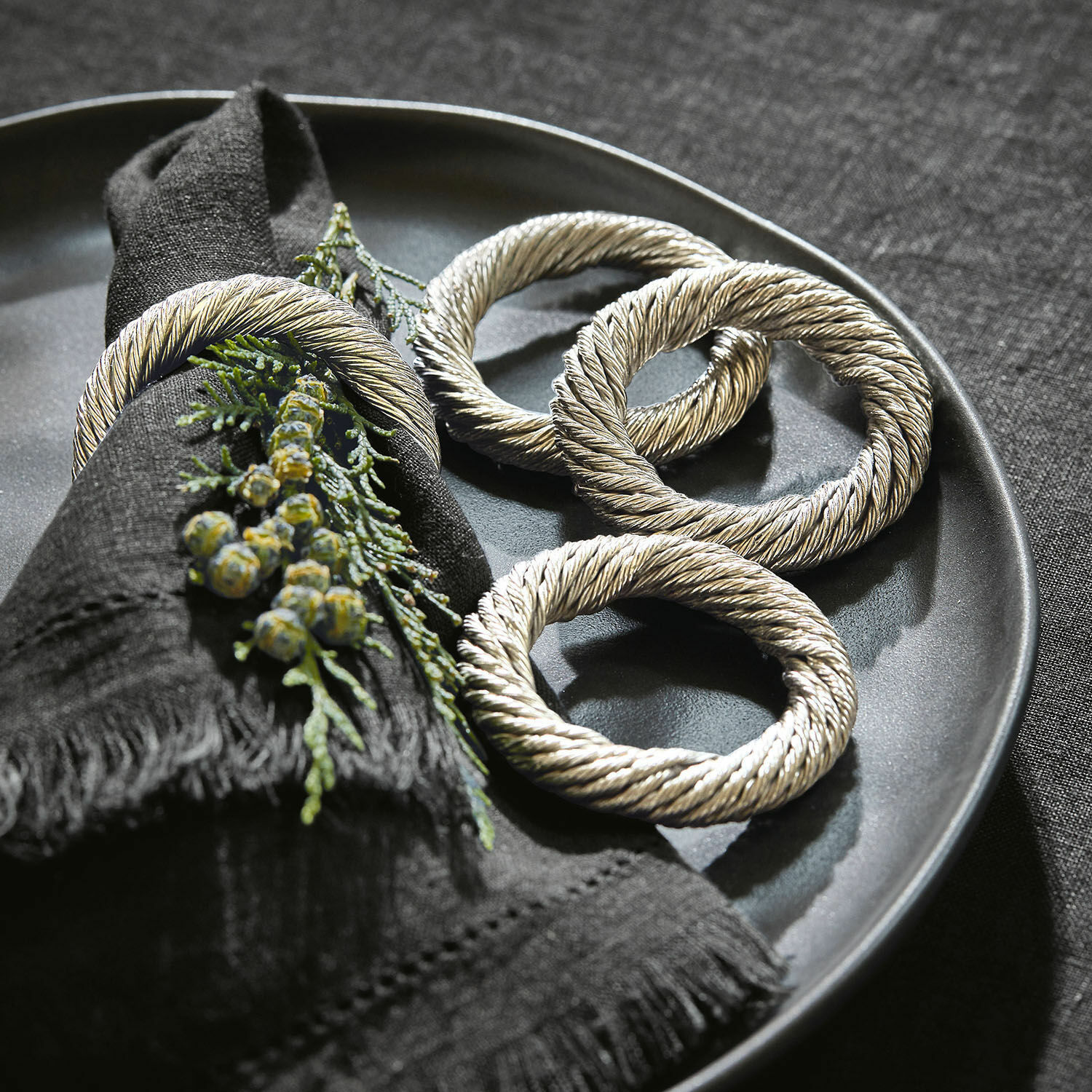 Lot de 4 ronds de serviettes Alea Anneaux de serviette en métal argenté sur une assiette noire avec décoration de branches vertes