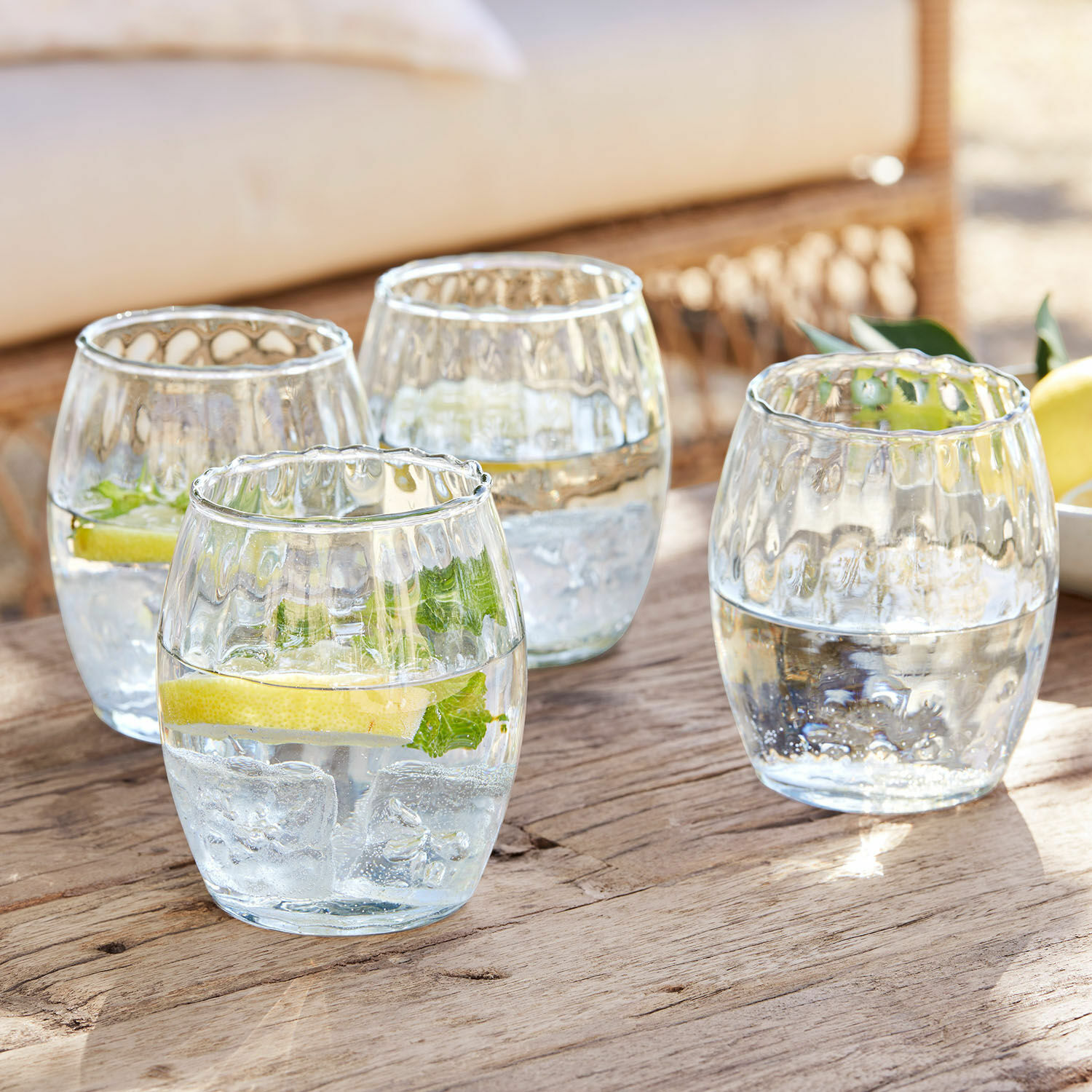 Lot de 4 verres Bourgavin Ensemble de quatre verres en verre transparent avec eau, glace et citron sur une table en bois