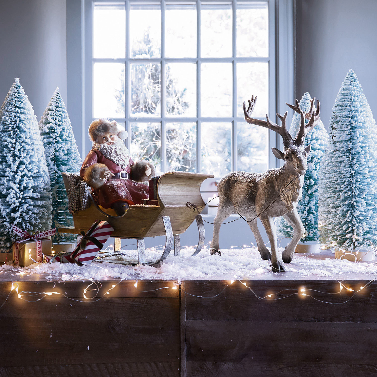 Traîneau du père Noël Palaima Figurine du Père Noël en manteau rouge sur traîneau en bois avec renne et sapins enneigés décoratifs