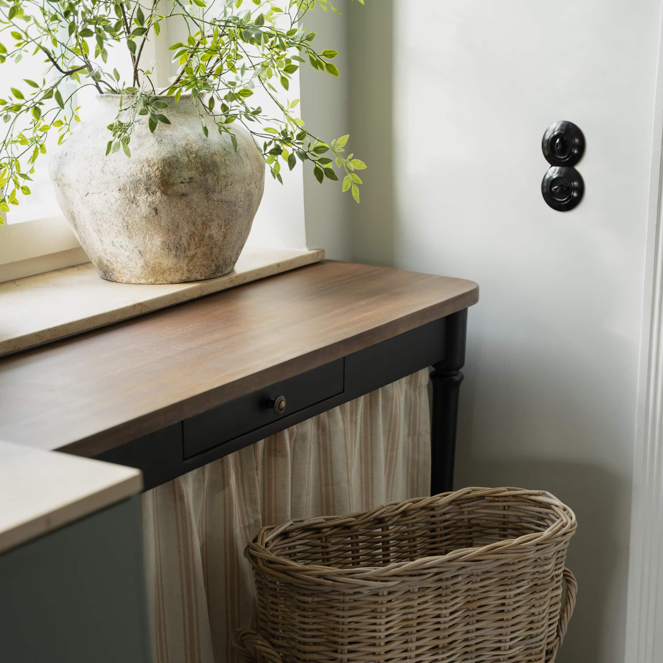 Vase rustique en pierre claire avec branches vertes sur un plateau de table en bois foncé