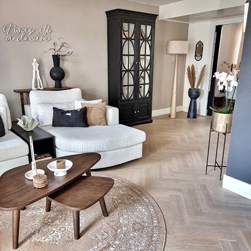 Salon chaleureux avec canapé gris clair, vitrine noire et table basse en bois sur tapis rond beige