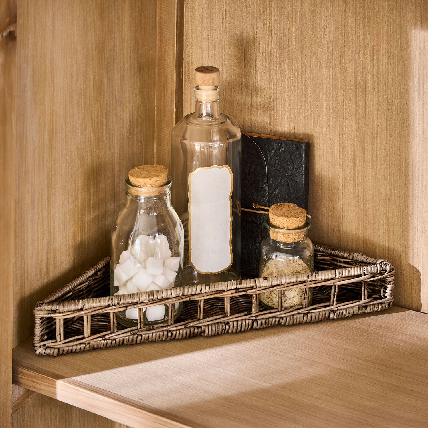 Panier d’angle Célunise Panier triangulaire en rotin naturel avec trois bouteilles en verre et un carnet sur une étagère en bois