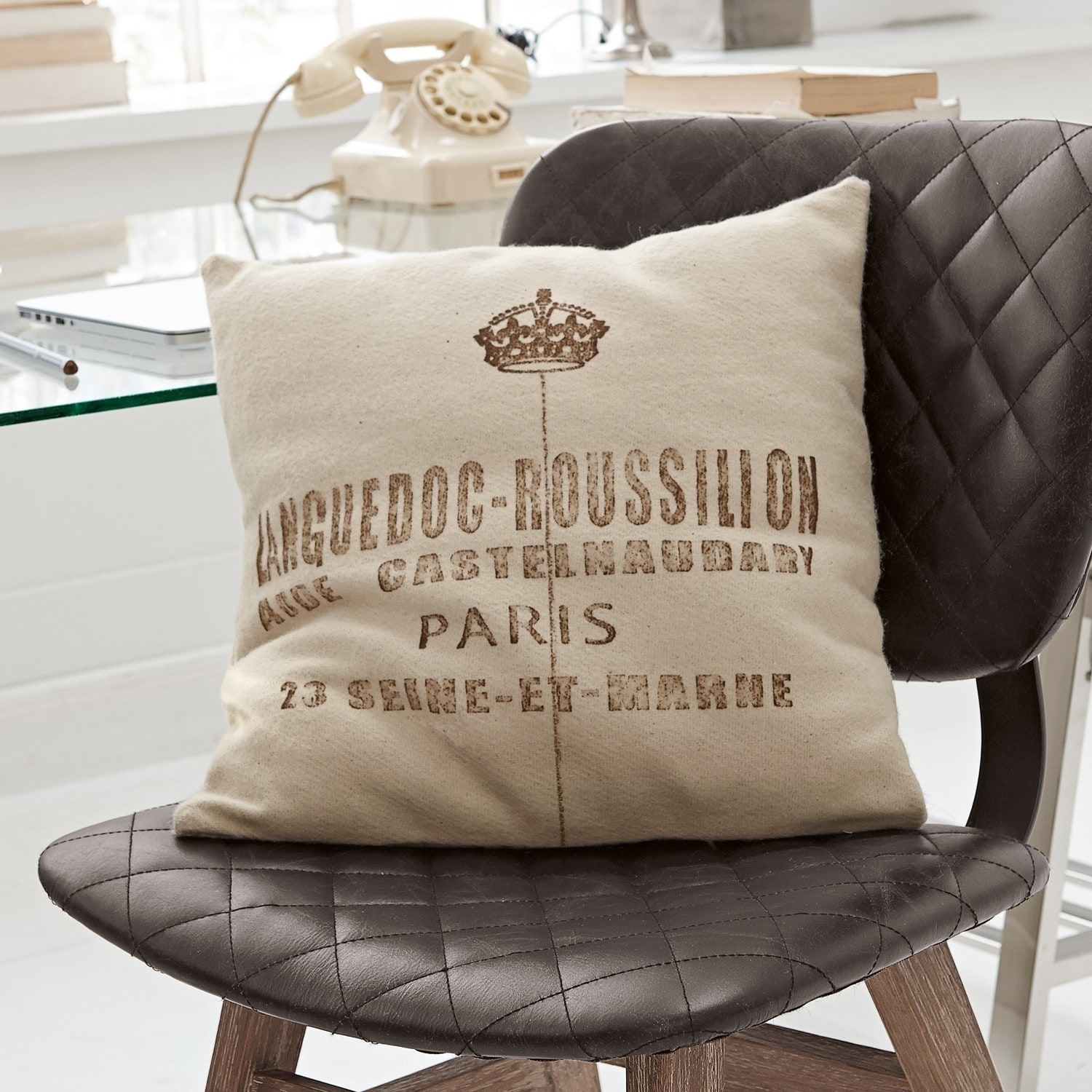 Coussin Roussilion Coussin beige avec impression Languedoc-Roussillon sur chaise noire matelassée en cuir