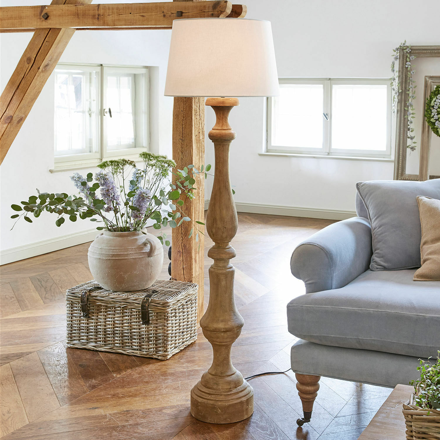 Lampadaire Etienne Lampadaire en bois avec abat-jour blanc dans un salon lumineux avec canapé bleu et panier en osier
